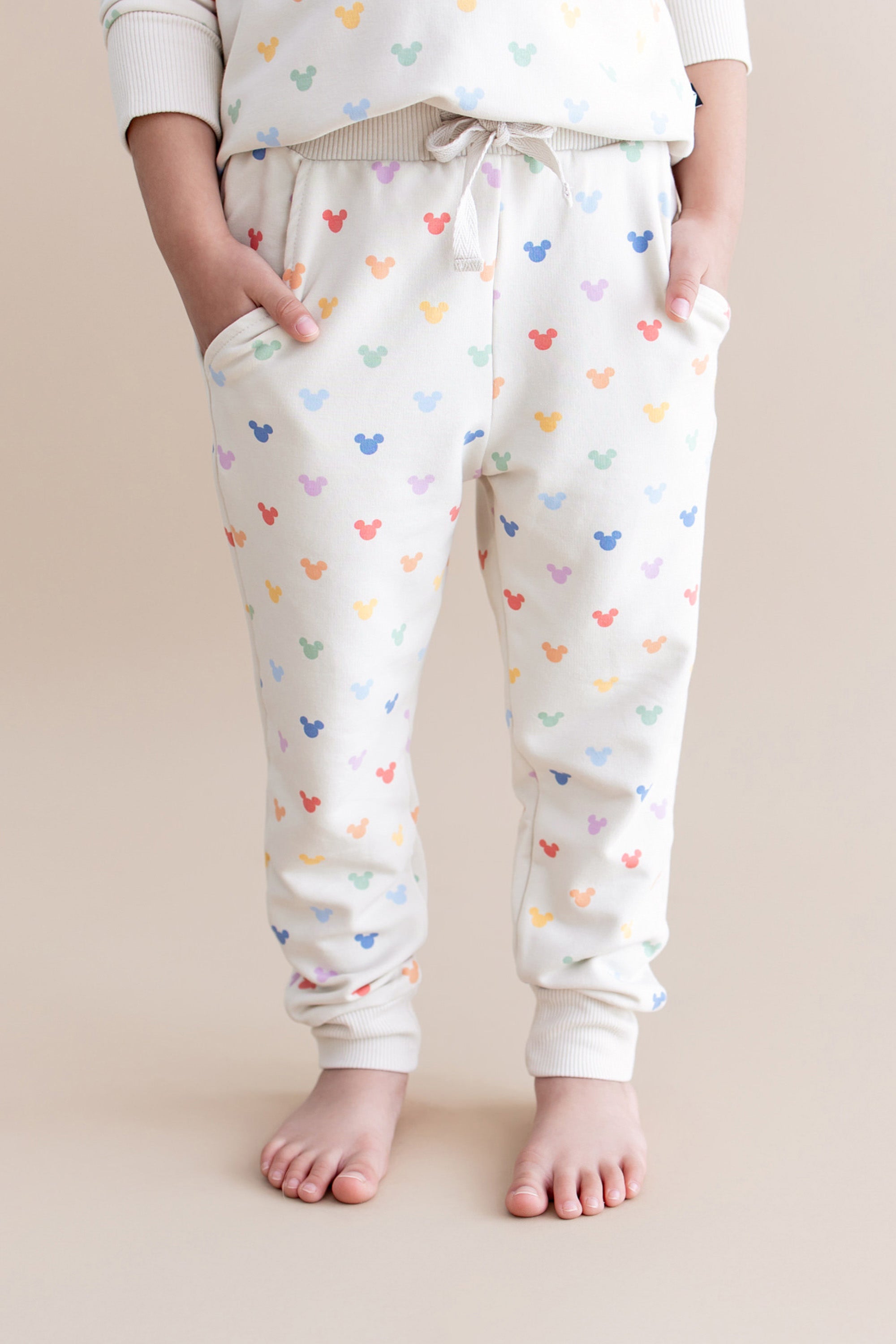 Child wearing jogger pants with colorful mickey pattern on a beige background
