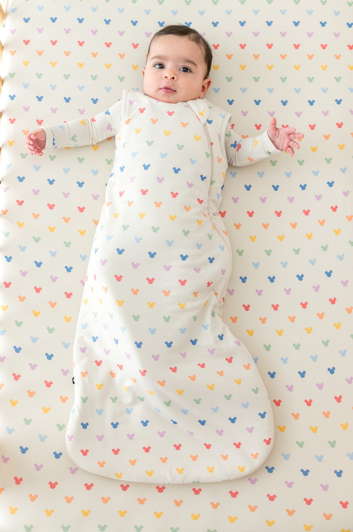 Baby in a crib with pastel mickey mouse head pattern and wearing a matching sleep sack