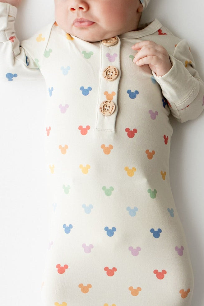 Newborn baby wrapped in a colorful mickey-patterned swaddle and wearing a matching hat on a white background