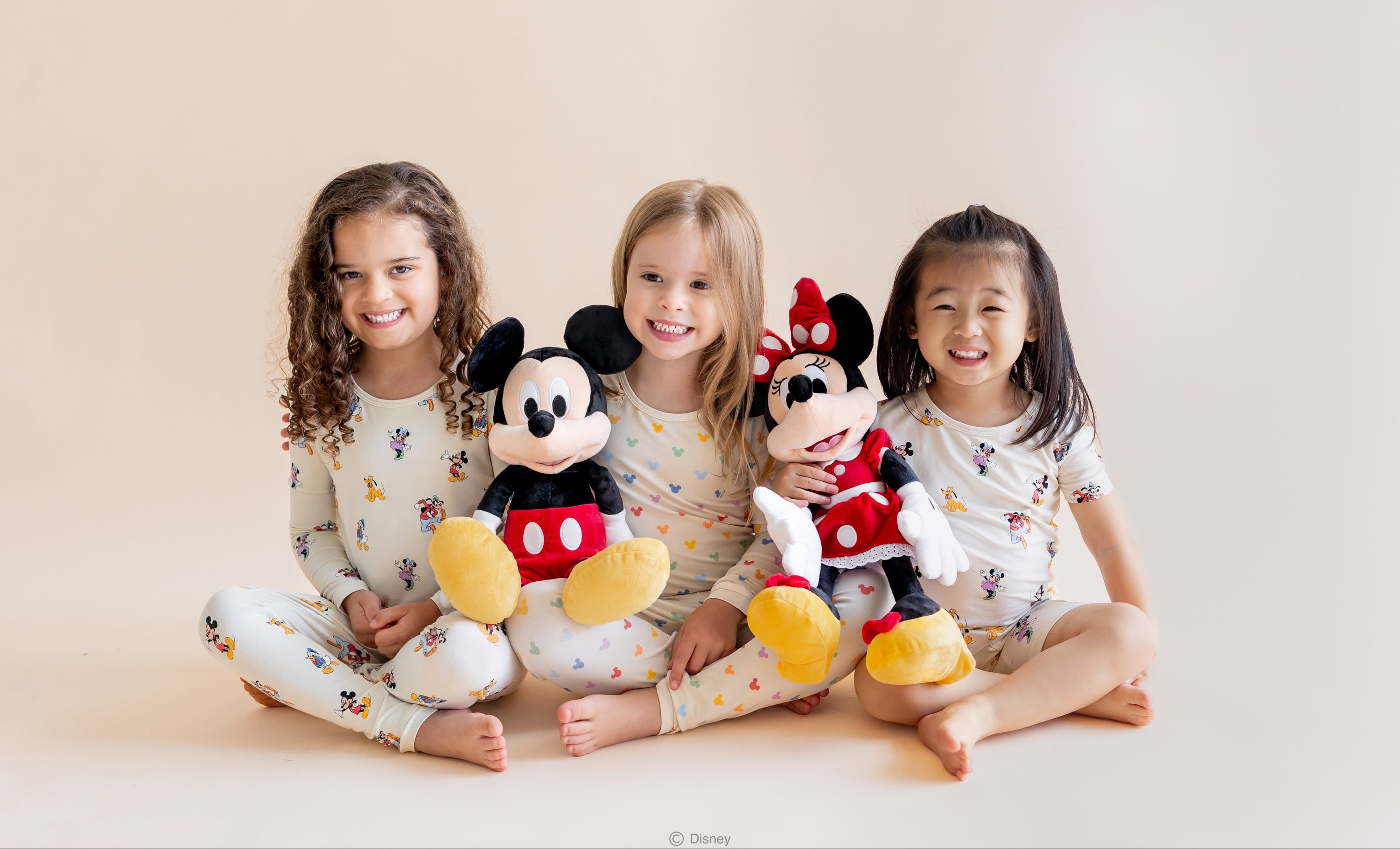3 kids sitting with mickey and friends printed pajamas holding mickey and minnie mouse stuffed characters