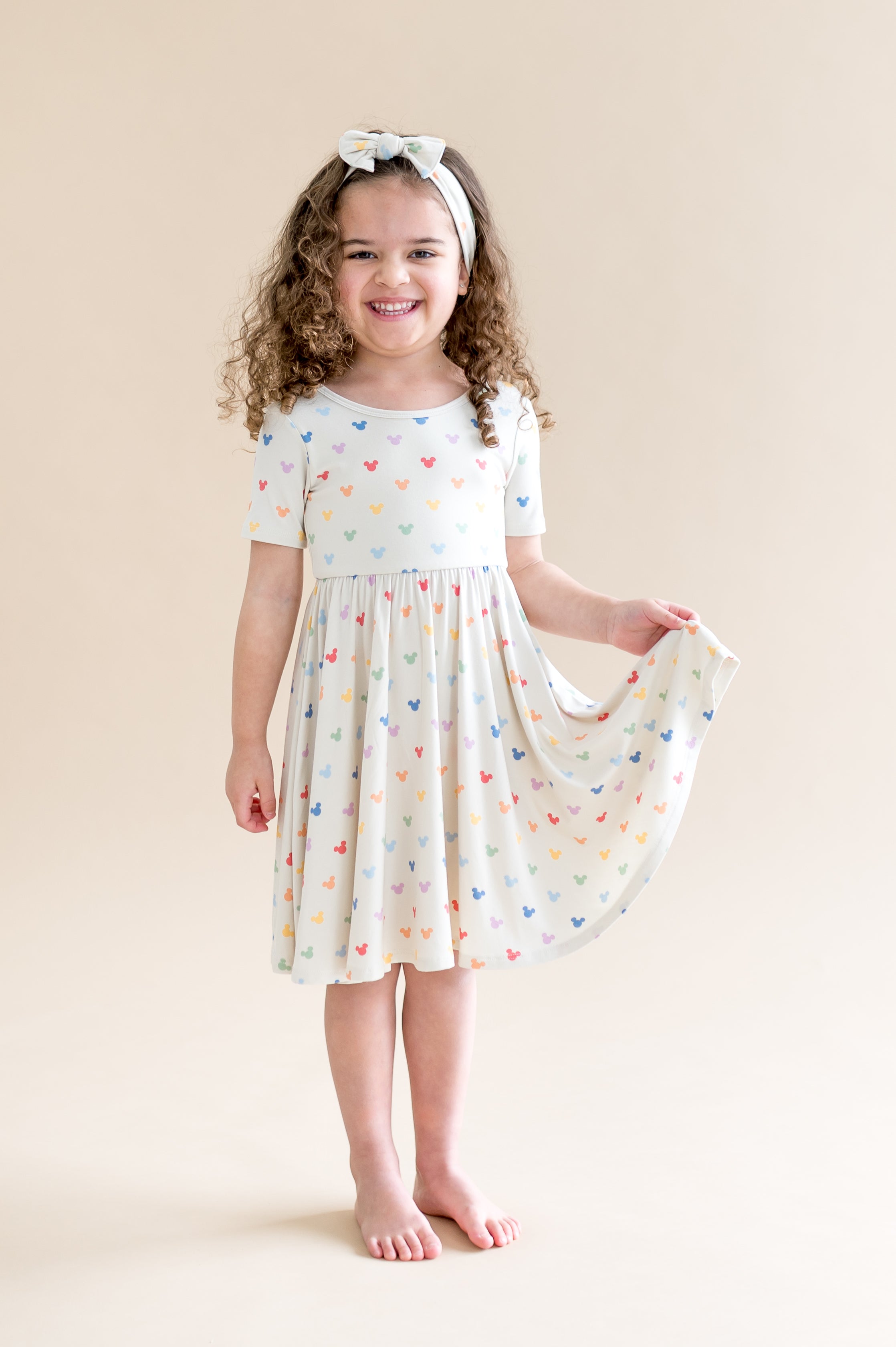 Girl in a short sleeve cream dress with colorful mickey mouse head pattern