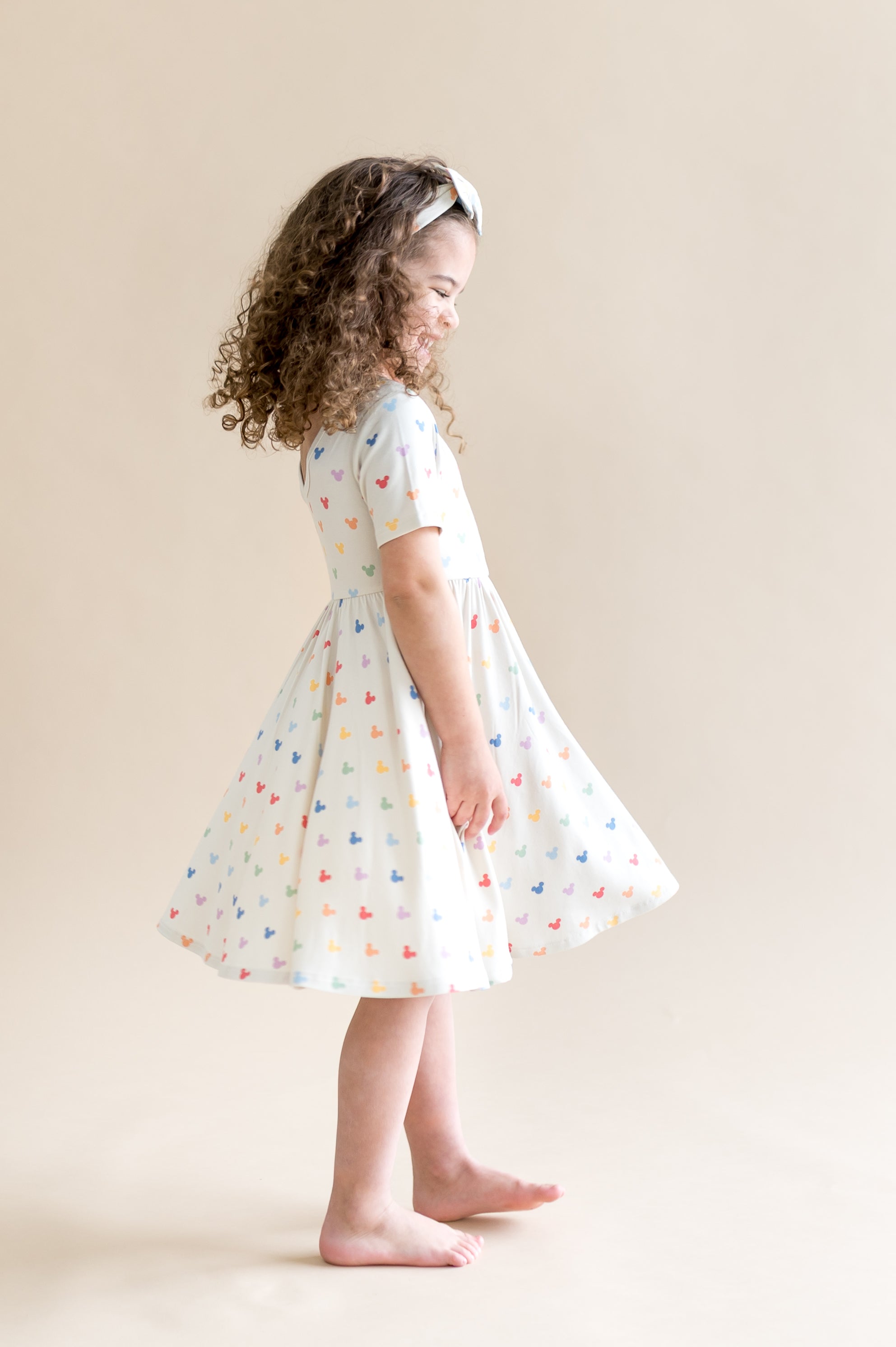 Girl twirling in a dress with colorful mickey mouse head pattern