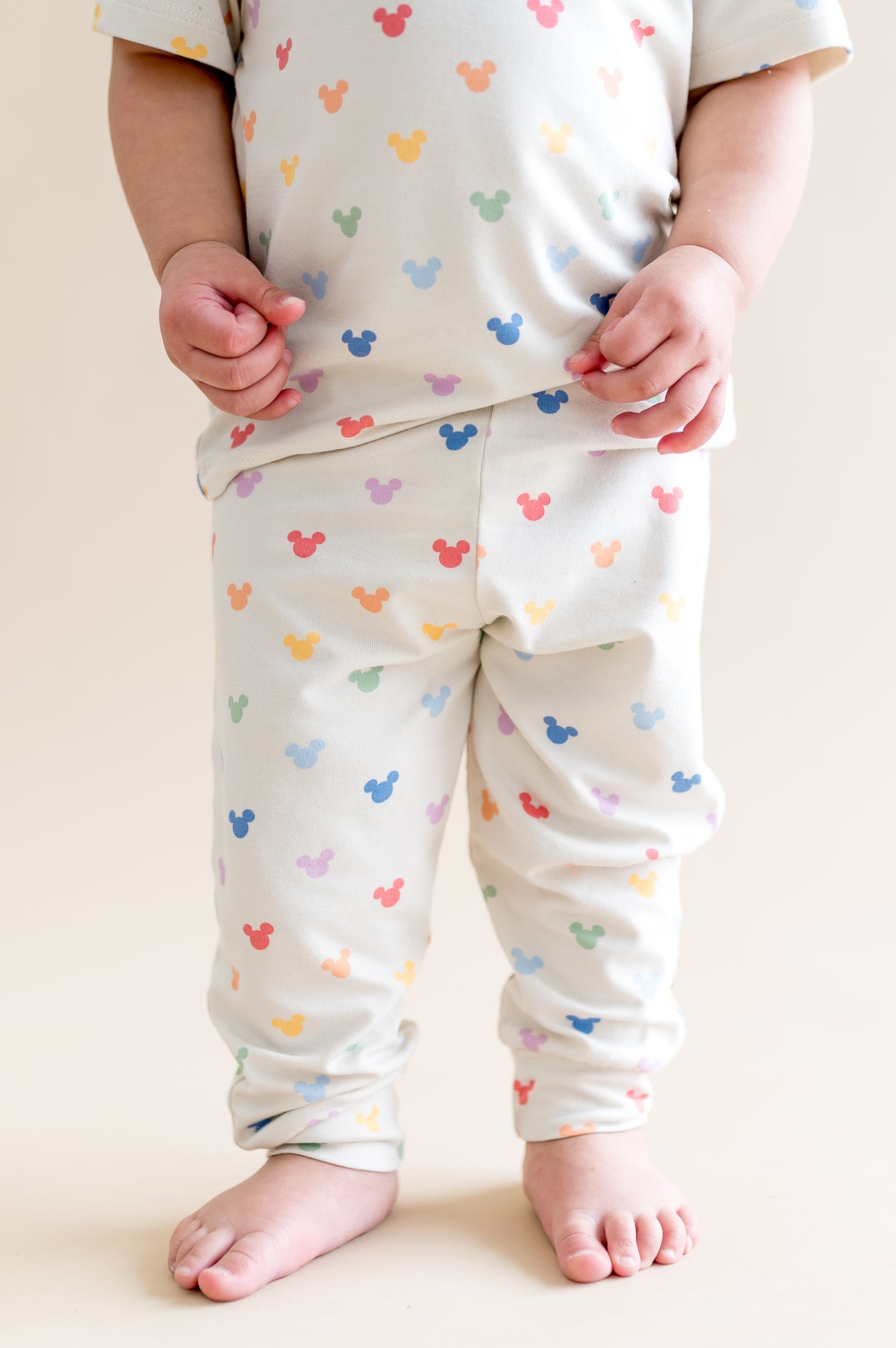 Child wearing pastel mickey head pattern pant on a plain background