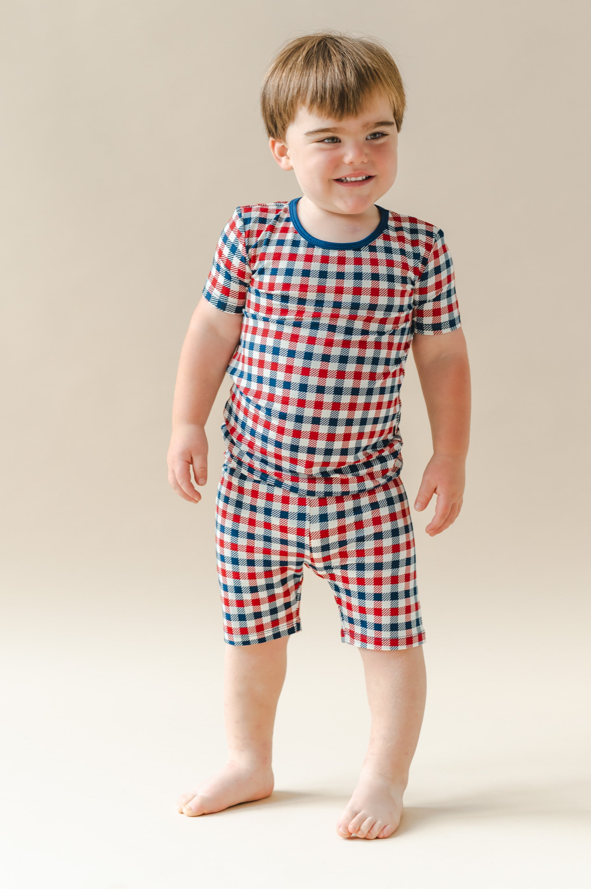 Child wearing Short Sleeve Pajamas in red blue and white Patriotic Gingham check print on a beige background