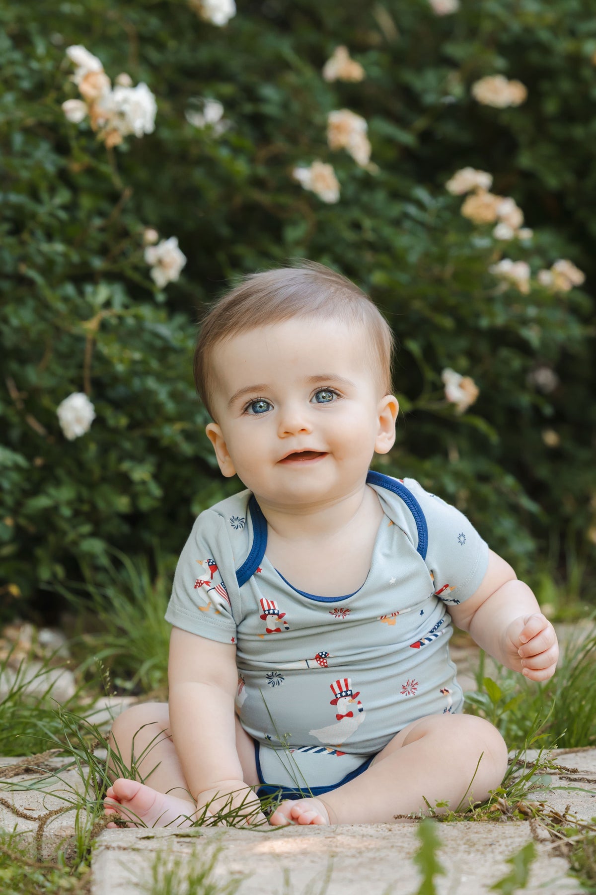 Baby sitting in Patriotic Goose print short sleeve bodysuit outdoors on a grass