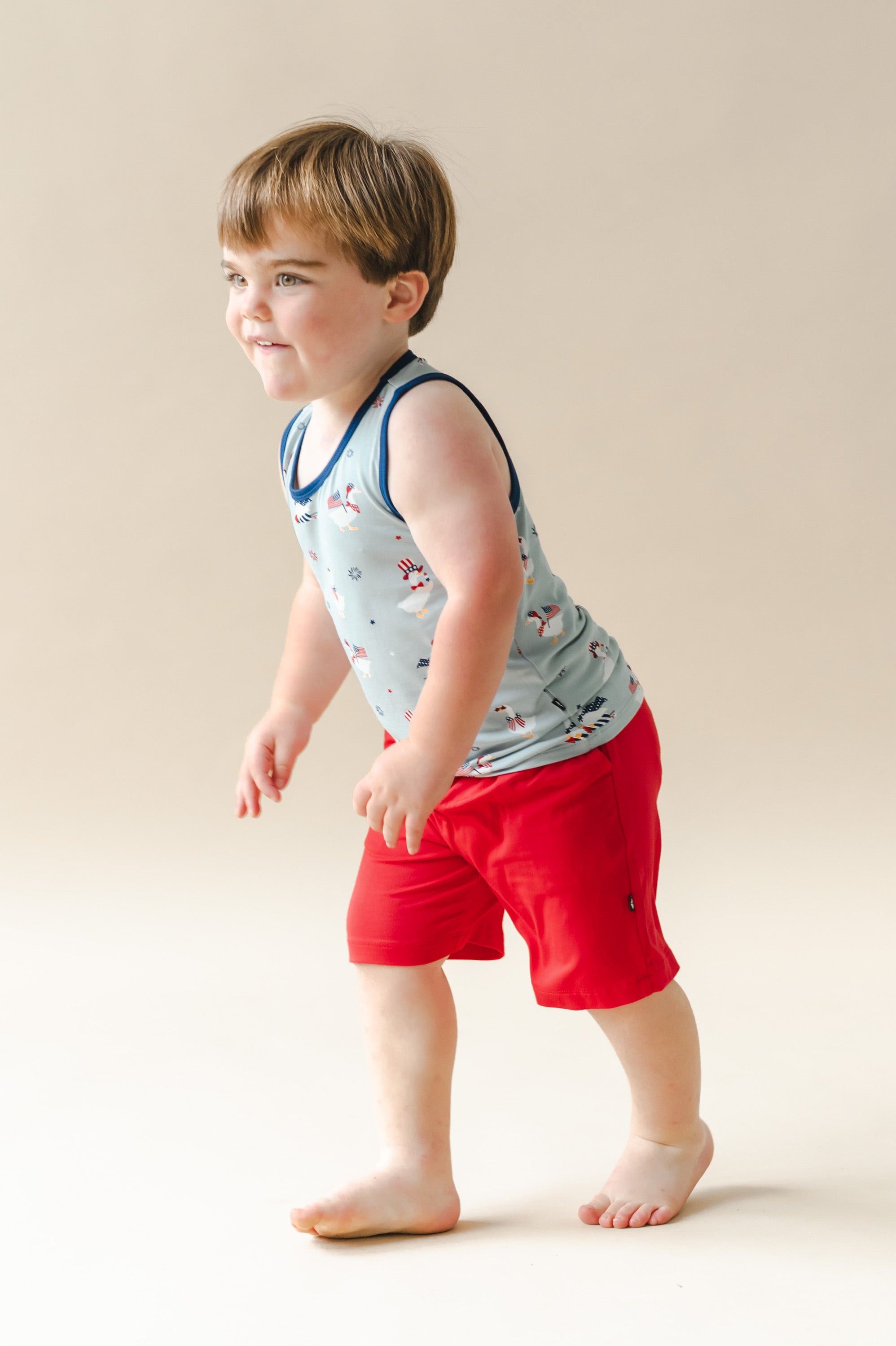 Child wearing a Light blue Toddler tank top in Patriotic Goose print with navy print over red shorts on a beige background