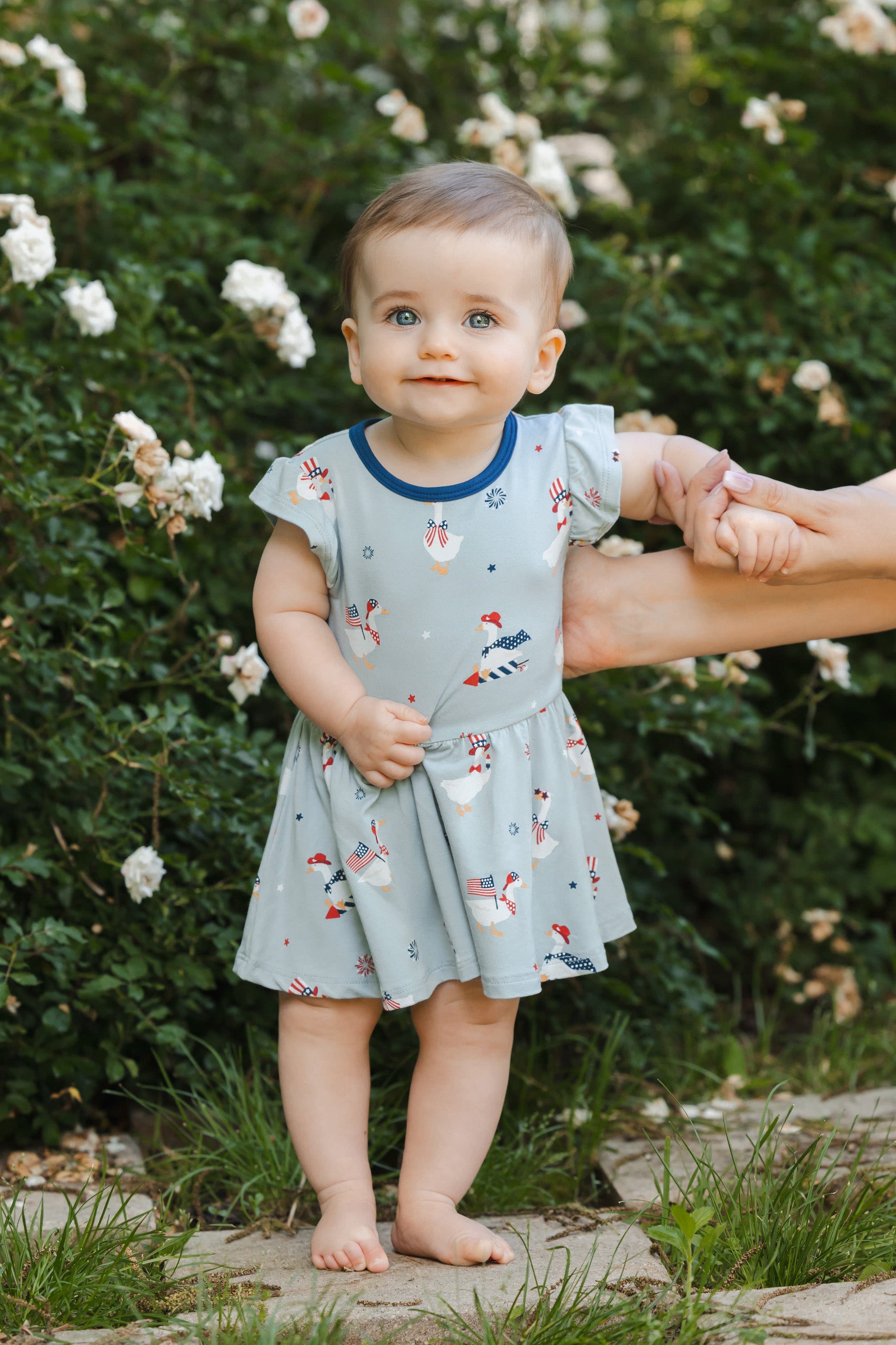 Baby wearing Light blue Twirl bodysuit dress in Patriotic Goose print outdoors