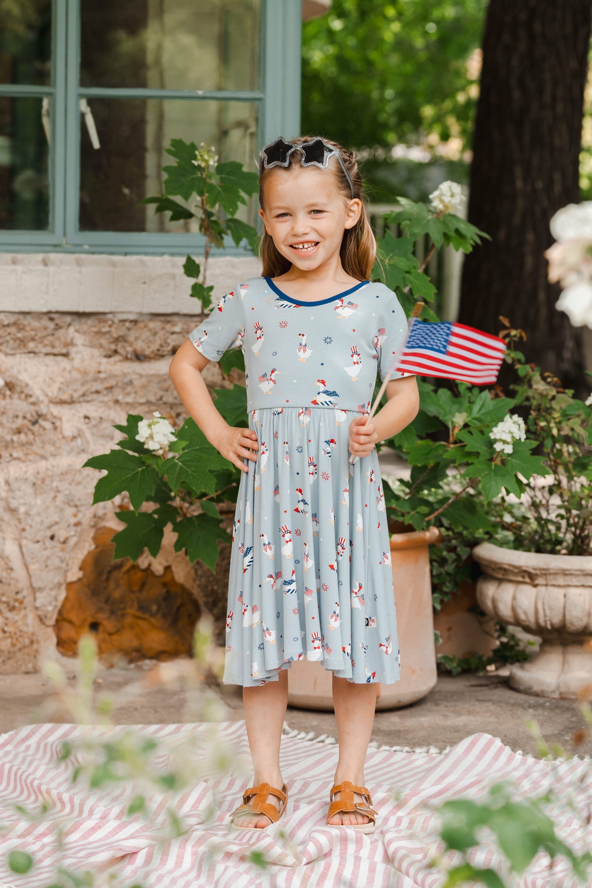 Child wearing Patriotic Goose print light blue Twirl dress with a flag outdoors
