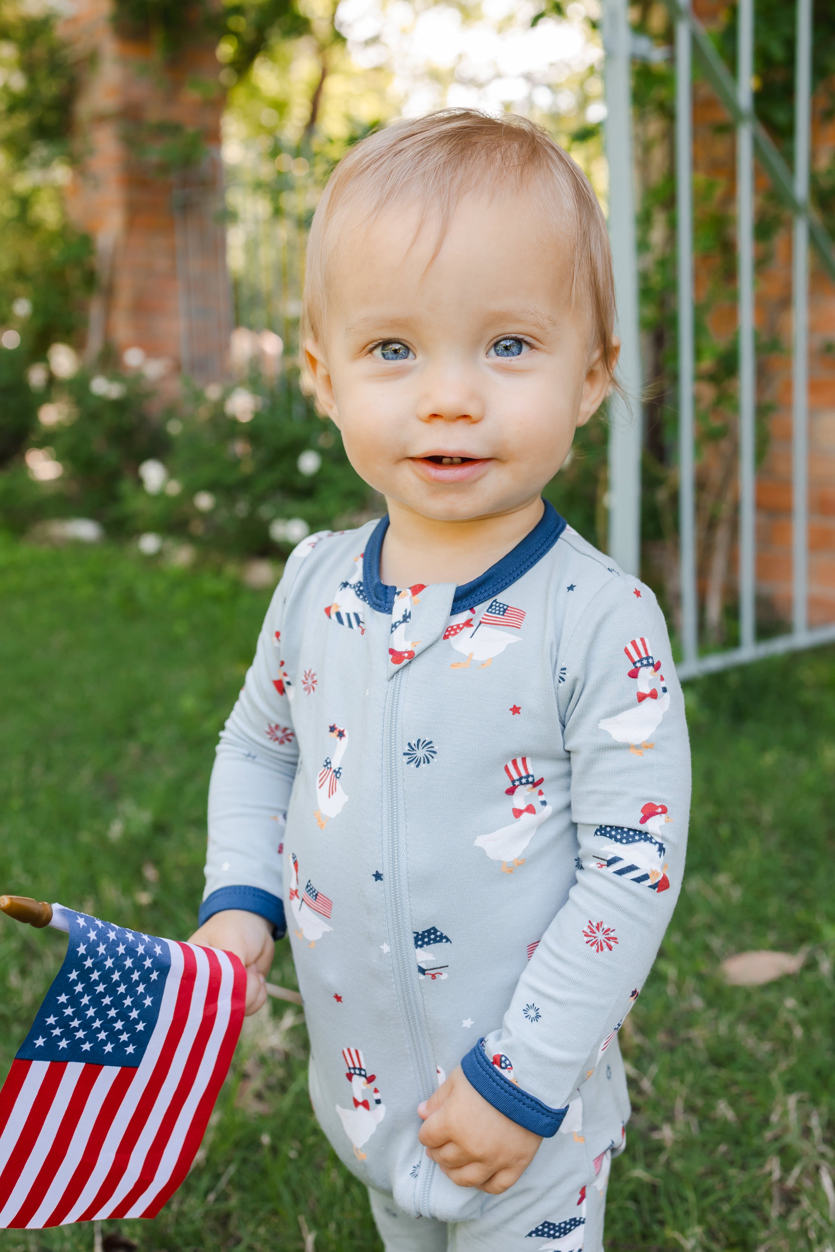 Child in Light blue zippered romper in Patriotic Goose print with a flag outdoors