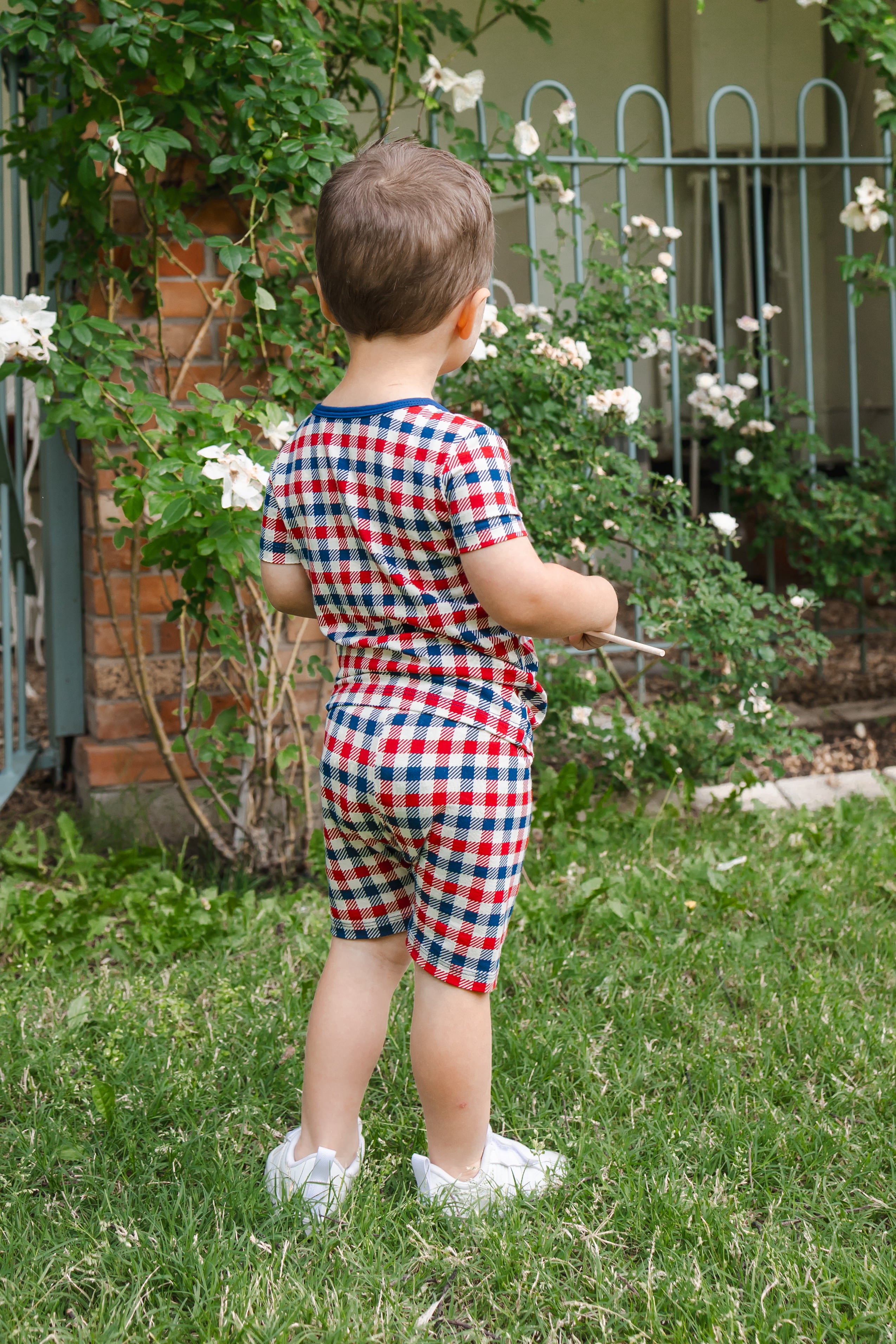 Back side of a child wearing Short Sleeve Pajamas in red blue and white Patriotic Gingham check print outdoors on a grass
