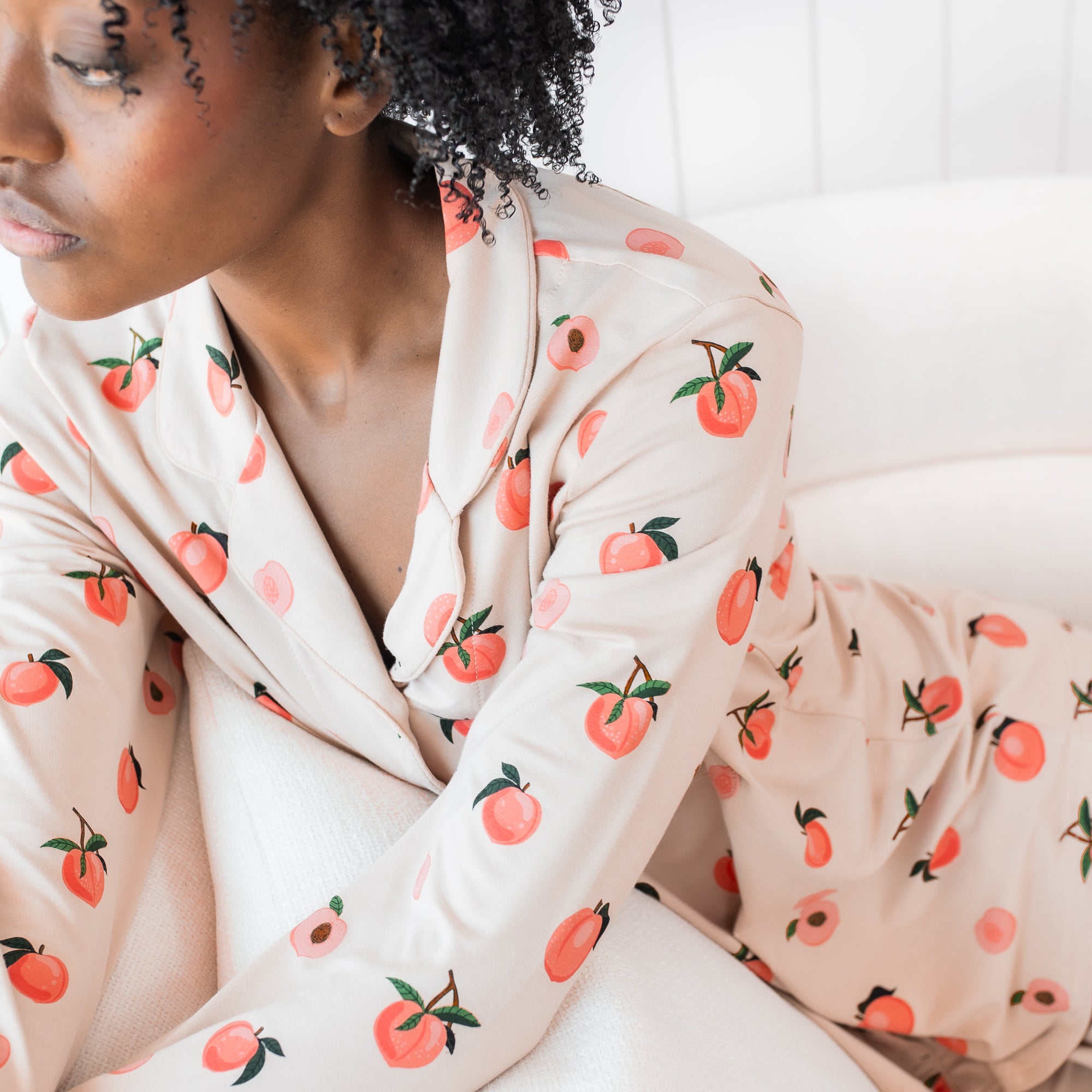 Woman modeling light pink button up bamboo pajamas in a peach print sitting in a chair