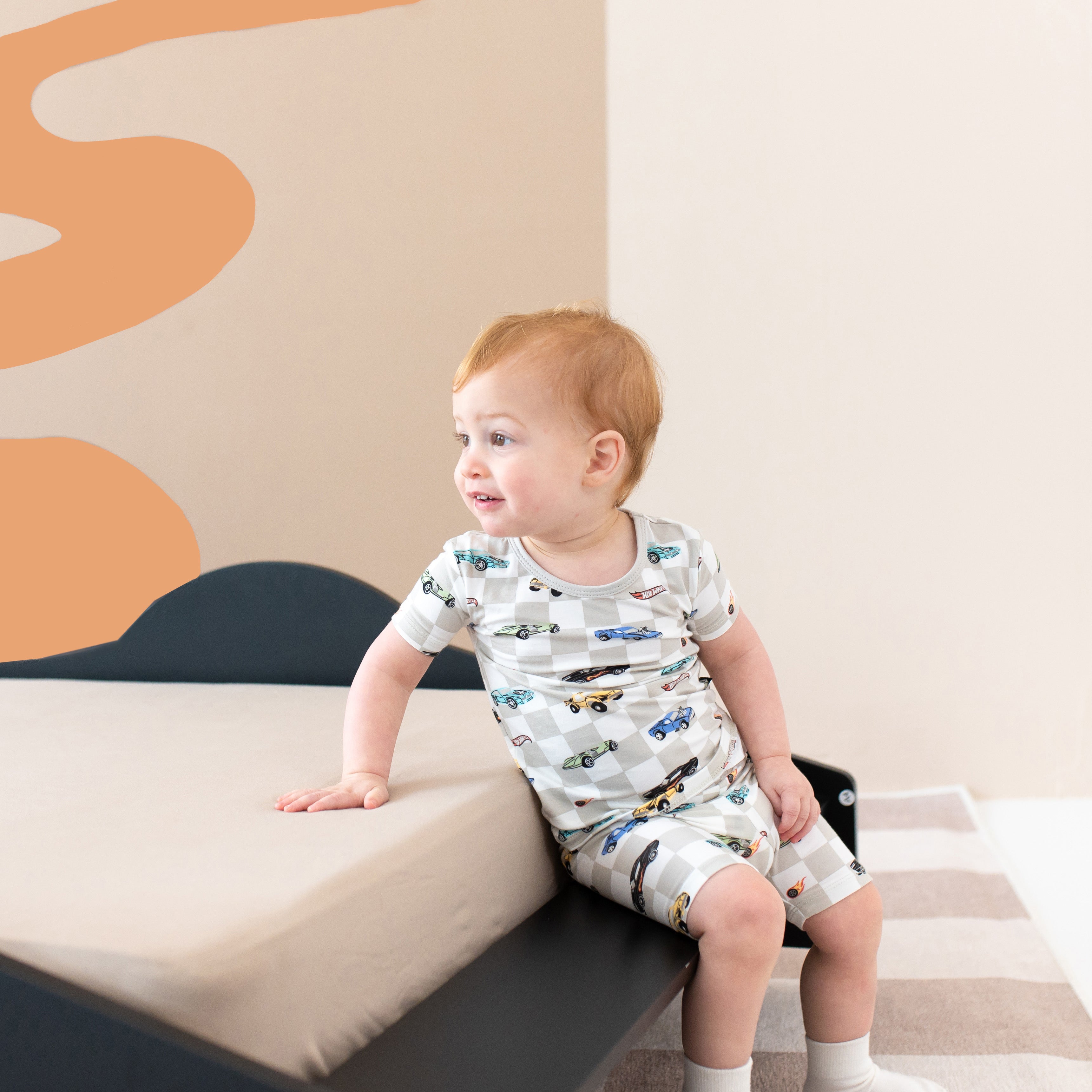 Toddler boy sitting on the edge of a car bed wearing the Short Sleeve Pajamas in Fast and Fierce