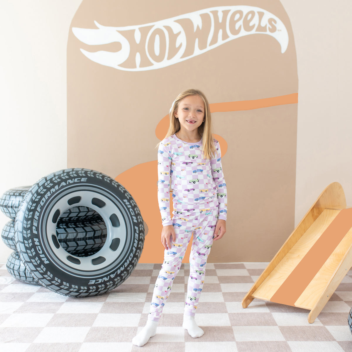 Girl model standing in front of the Hot Wheels™ backdrop wearing the Long Sleeve Pajamas in Sparkles and Speed