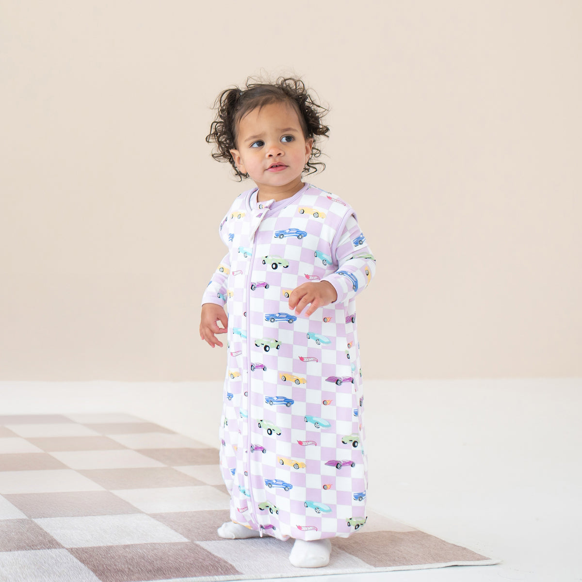 Young toddler standing wearing the Sleep Bag Walker in Sparkles and Speed 1.0 with matching romper on underneath