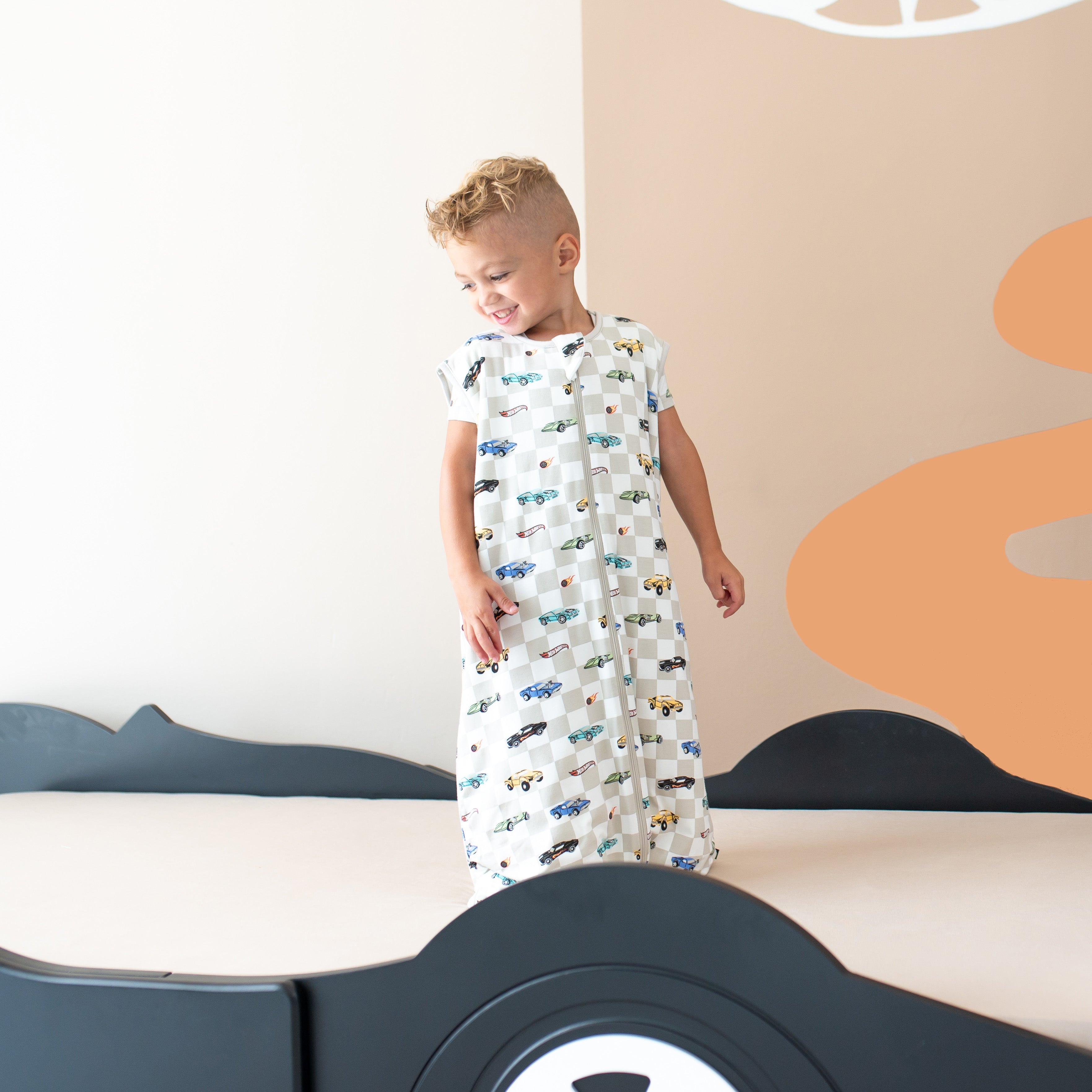 Child laughing while standing on a bed wearing the Sleep Bag Walker in Fast and Fierce 1.0