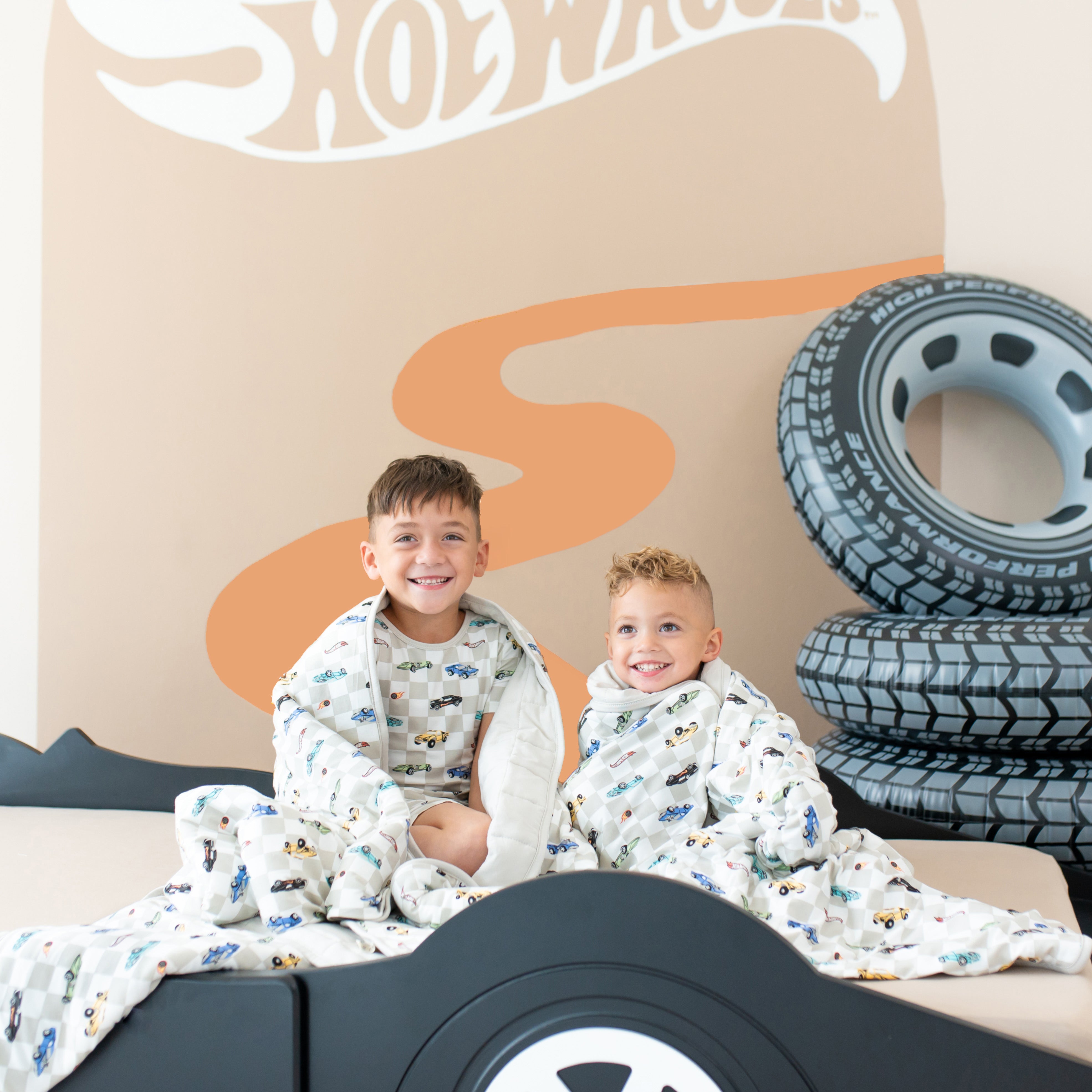 Two child models sitting on a bed with a Youth and Toddler Blanket in Fast and Fierce wrapped around each of them