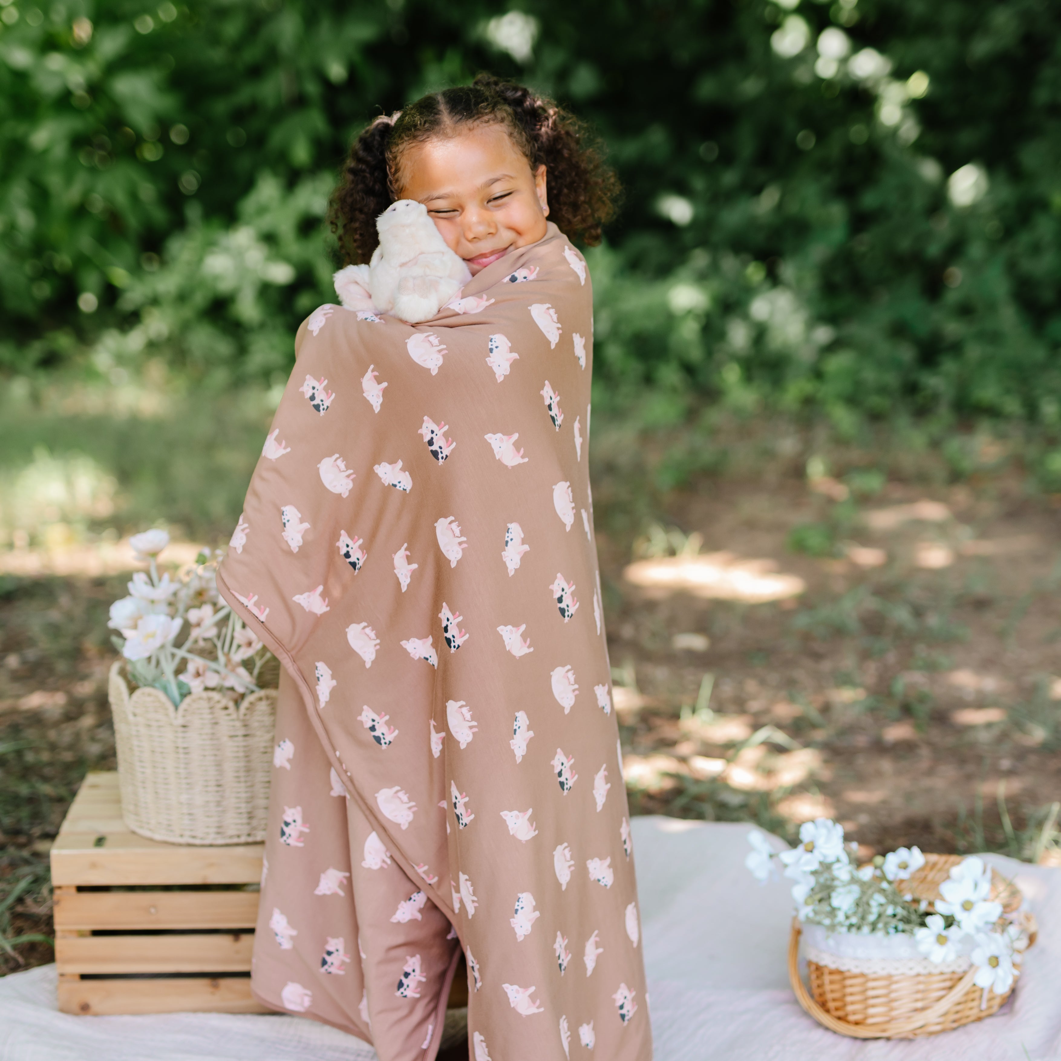 Girl wrapped in Toddler Blanket in Pig TOG 1.0 cuddling a stuffed pig