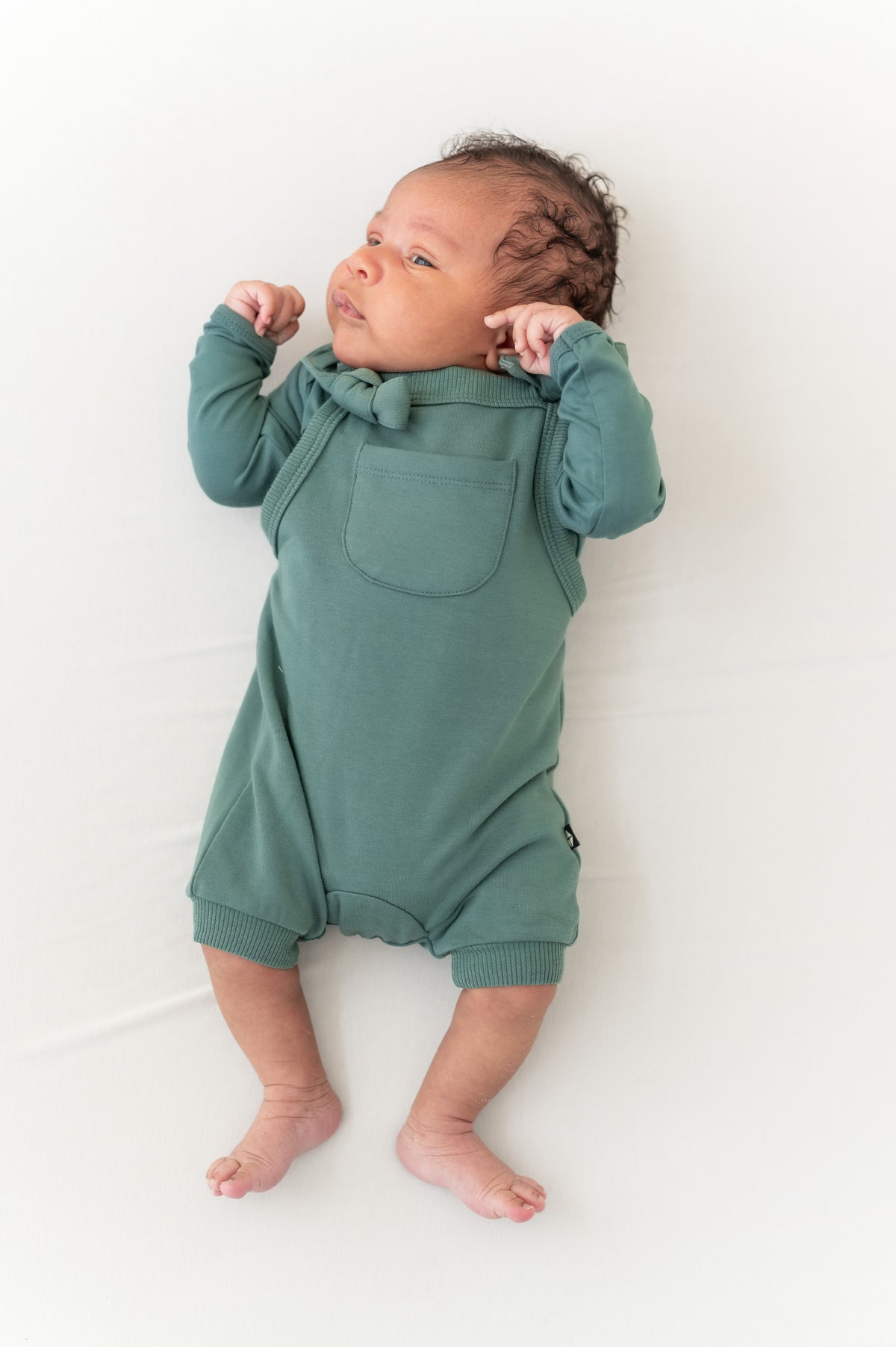 Baby wearing Overall in Pine color over similar color shirt on a beige background