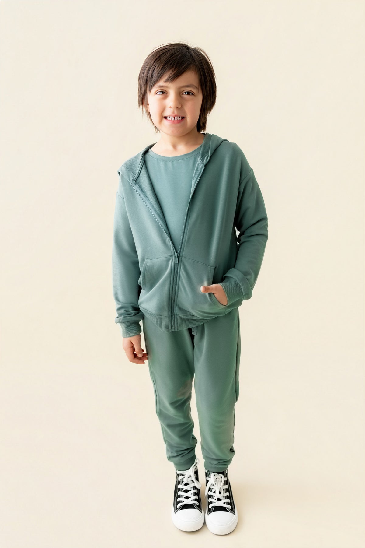Boy smiling in Jogger Pant in Pine color under pine color Zip up hoodie on a beige background