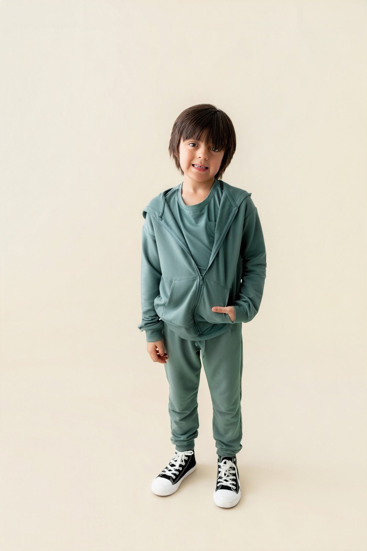 Boy wearing Jogger Pant in Pine color under pine color Zip up hoodie on a beige background