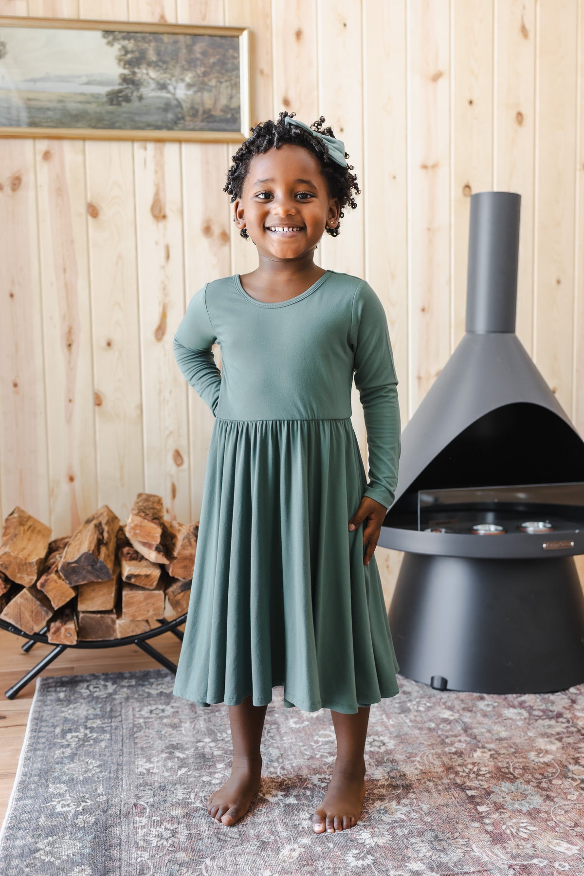 Girl posing in Long Sleeve Twirl Dress in Pine standing near chimney