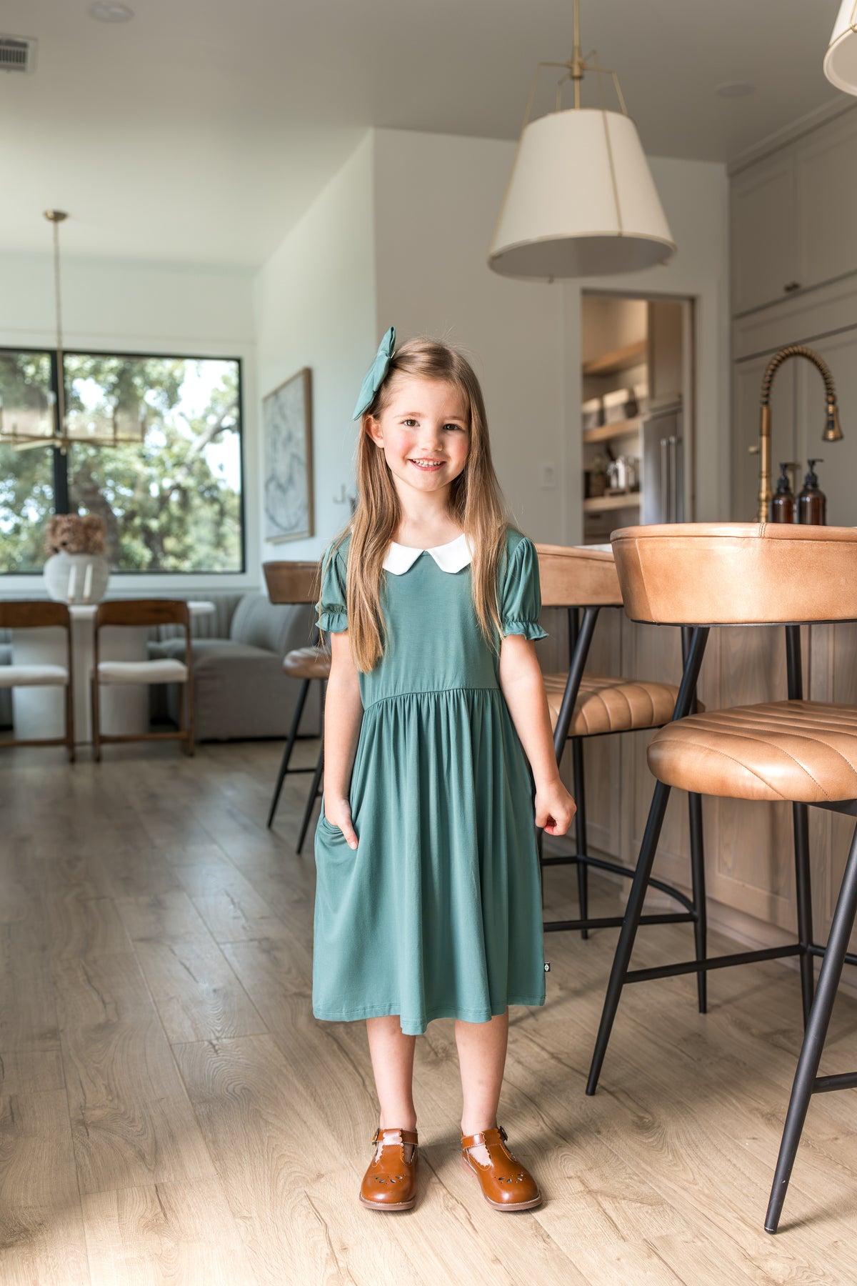Girl wearing Peter Pan Collar Dress in Pine while standing near chairs