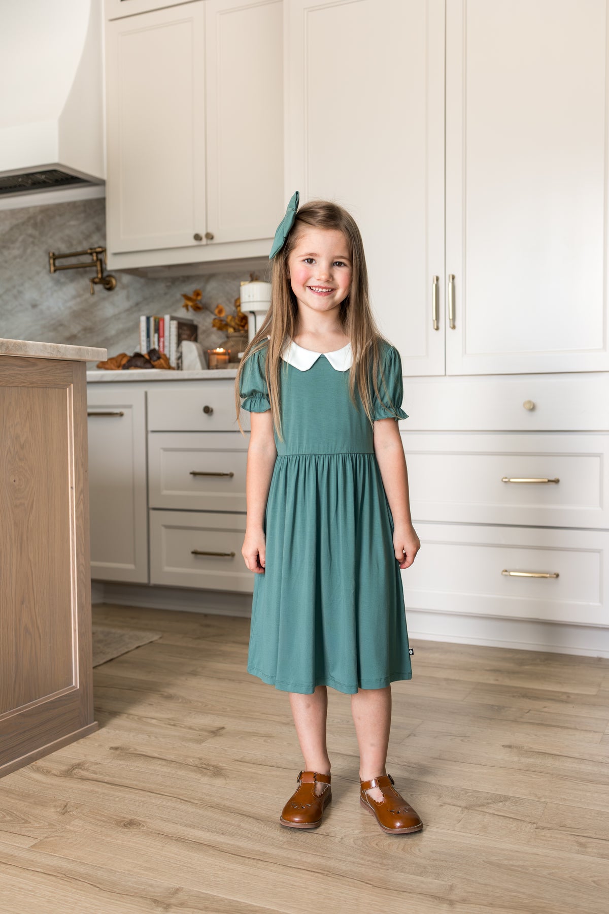 Girl wearing Peter Pan Collar Dress in Pine while standing in kitchen