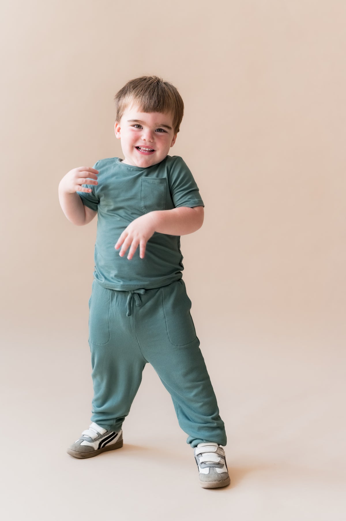 Child smiling in Ribbed Jogger Pant in Pine on a beige background