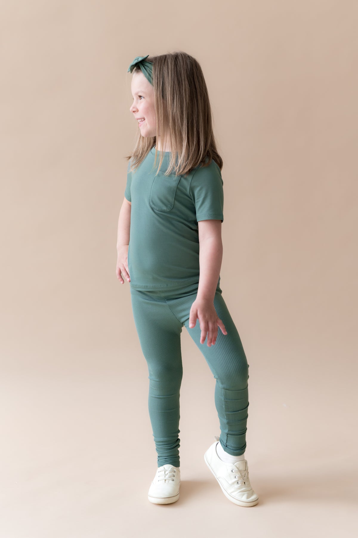 Girl posing in Ribbed Leggings and knotted bow headband in Pine on a beige background