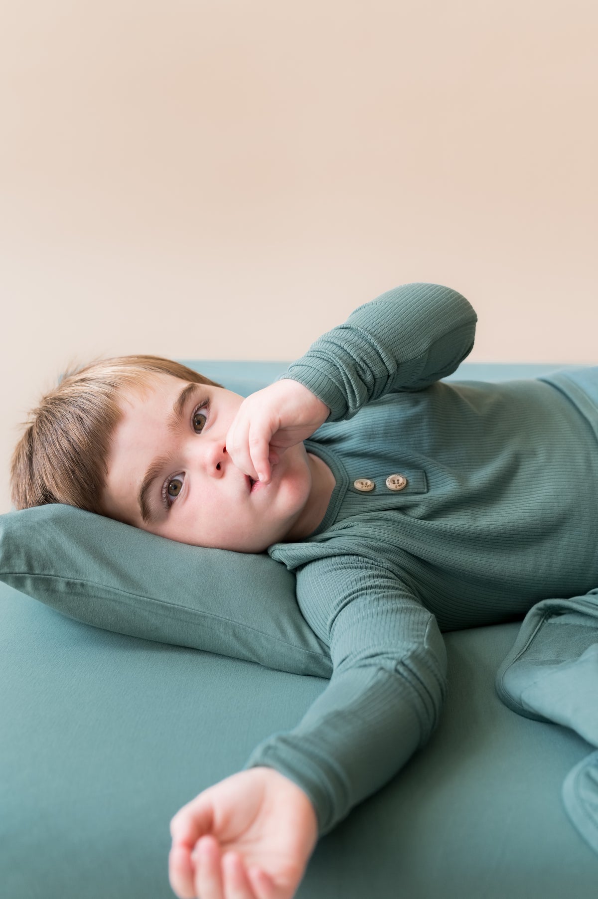 Boy lying on Toddler Pillowcase in Pine while wearing pine shirt on pine sheet