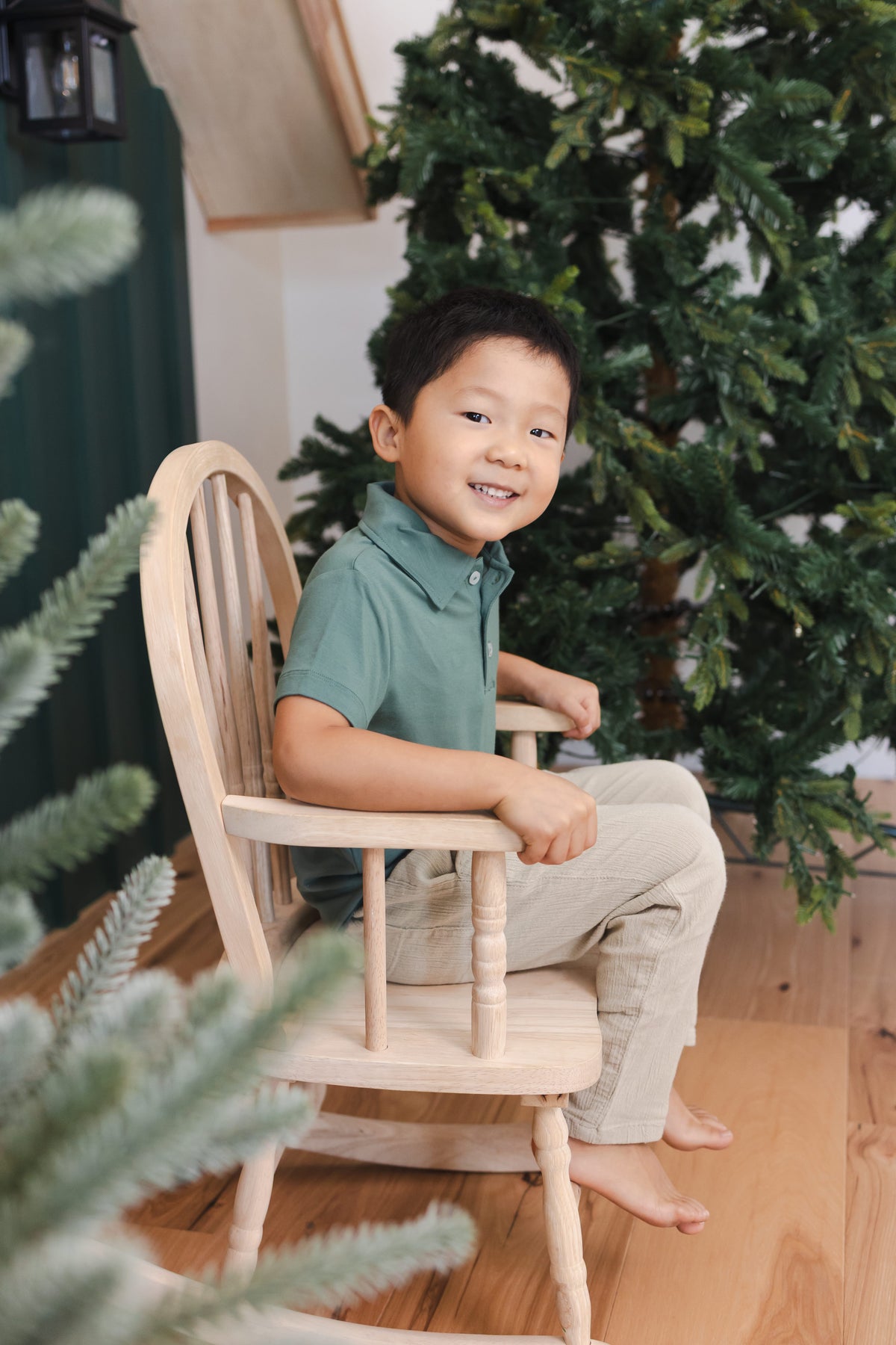 Toddler sitting on a chair wearing Toddler Short Sleeve Polo in Pine over off white pants