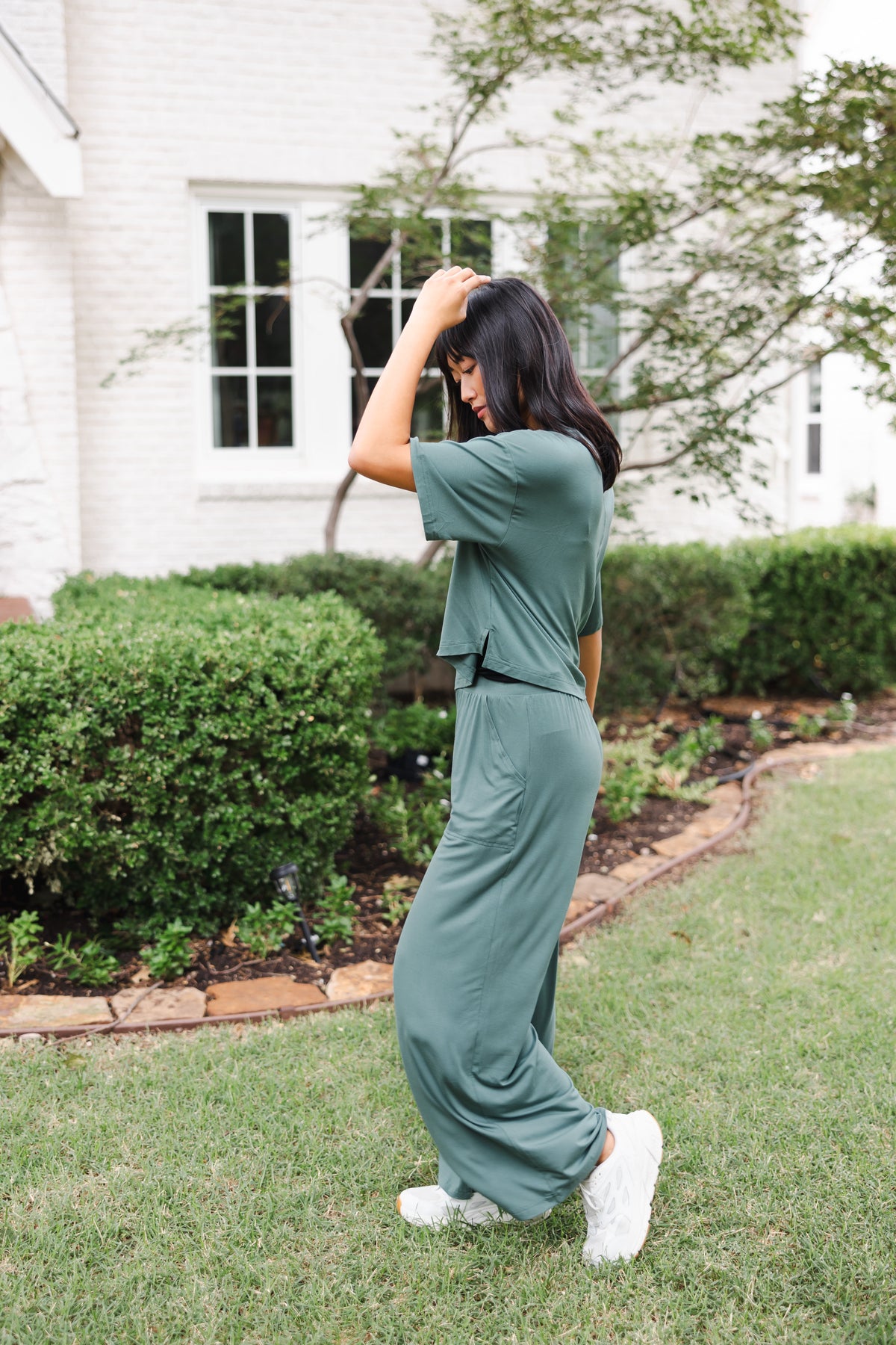 Female model posing in a garden outdoors wearing the Women's Wide Leg Pant in Burgundy and matching short sleeve tee over white shoes