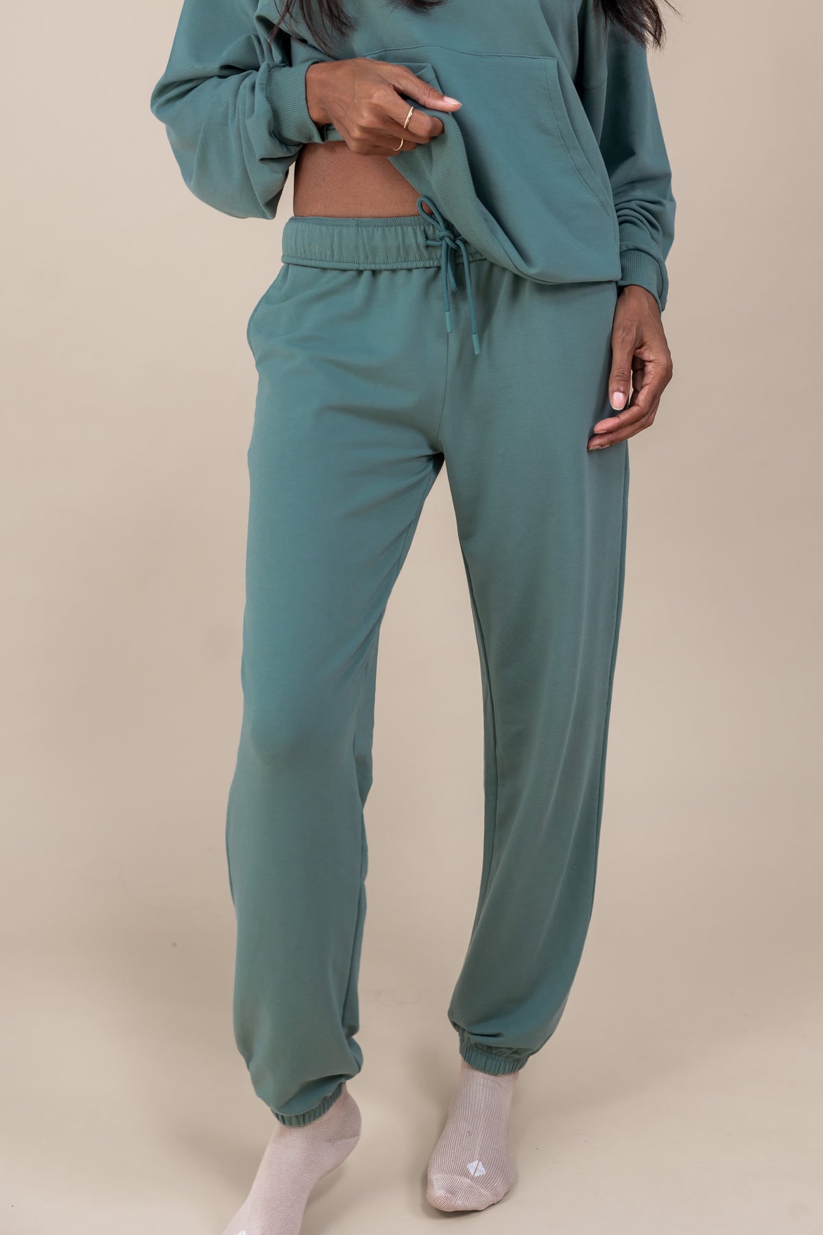 Modal wearing Women's Jogger Pants in Pine color under similar color women's hoodie on a beige background
