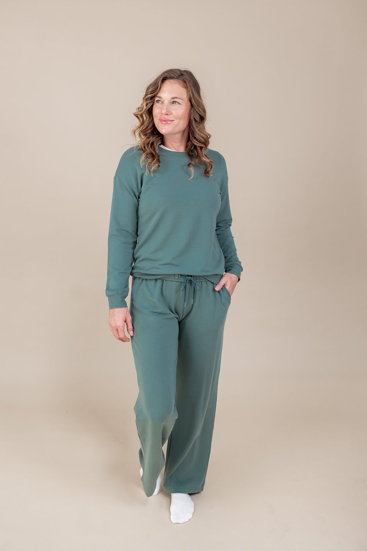 Woman posing in Women's Sweatshirt in Pine color over Women's sweatpants in pine on a beige background