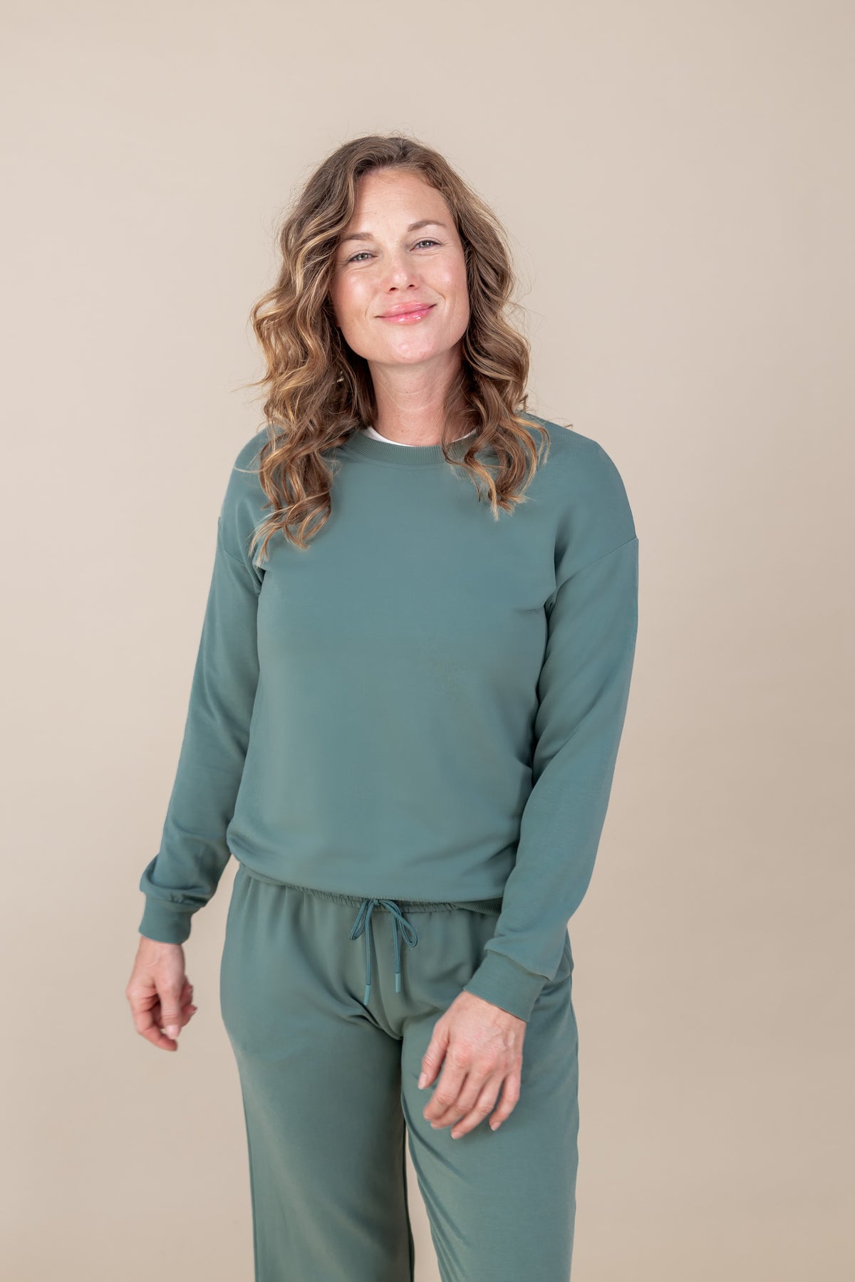 Woman wearing Women's Sweatshirt in Pine color over Women's sweatpants in pine on a beige background