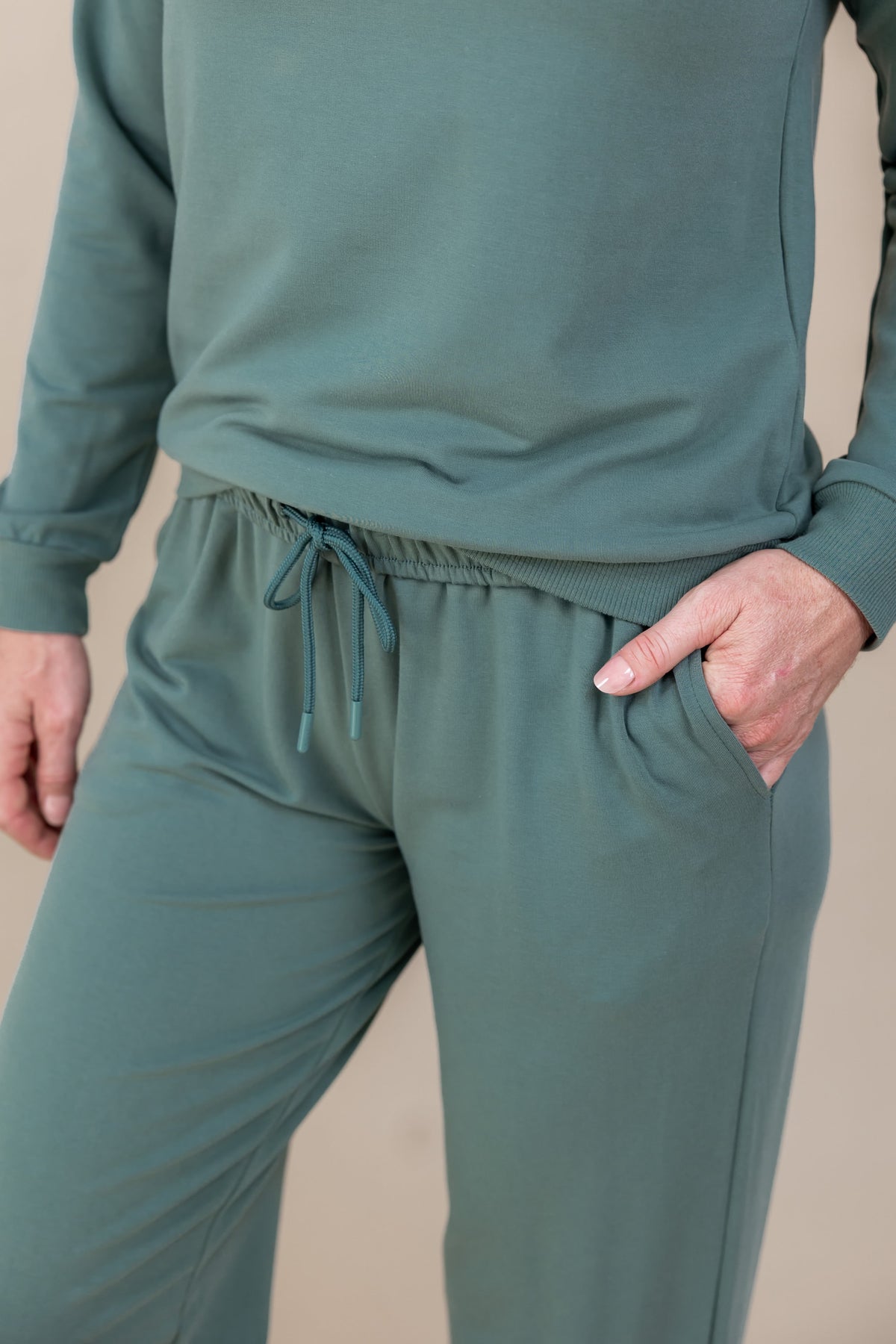 Woman posing in Women's Sweatshirt in Pine color over Women's sweatpants in pine with pockets on a beige background