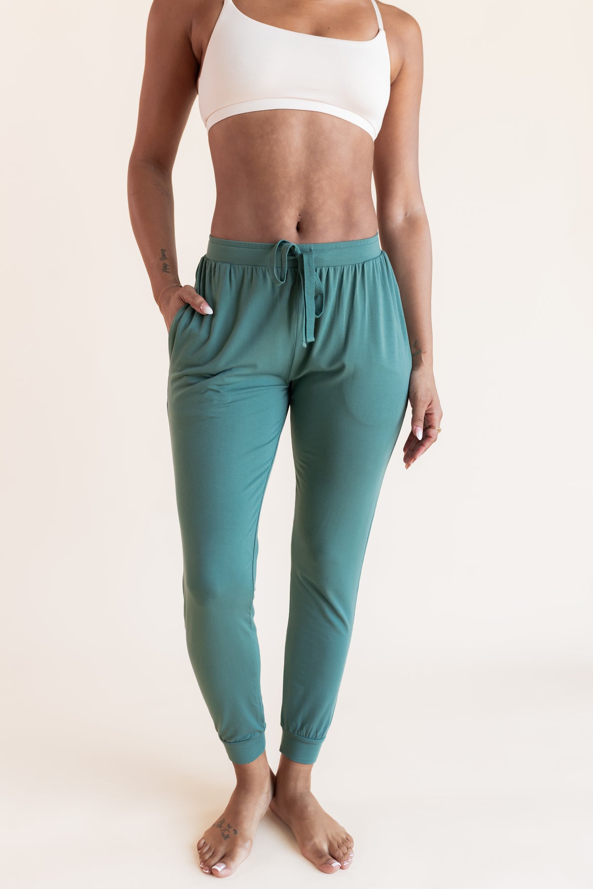 Model wearing Women's Jogger Pants in Pine under white bralette on a beige background