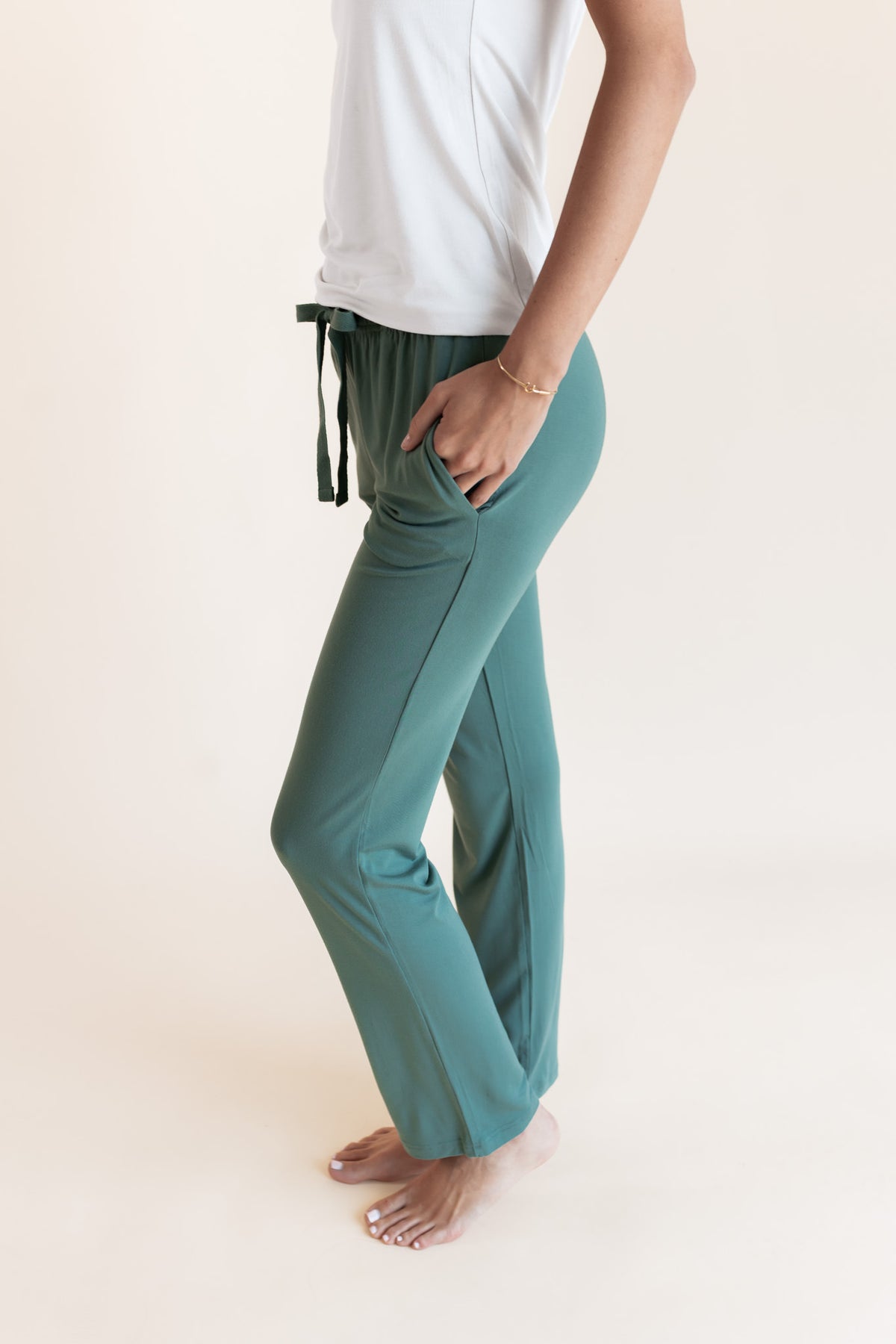 Model showcasing Women's Lounge Pants in Pine with pockets under white camisole on a beige background