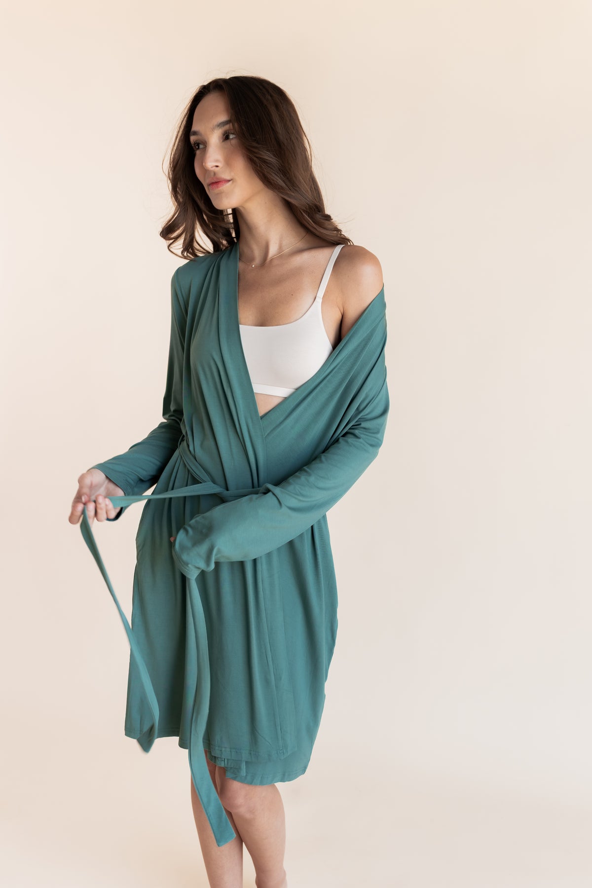 Model wearing Women's Lounge Robe in Pine with belt over white bralette on a beige background