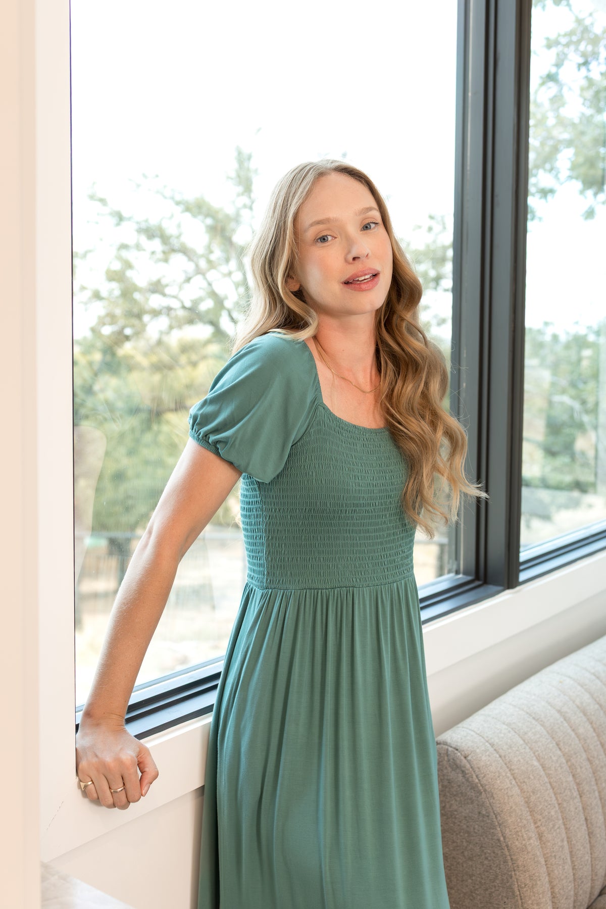Model wearing Women’s Smocked Dress in Pine standing in a living room