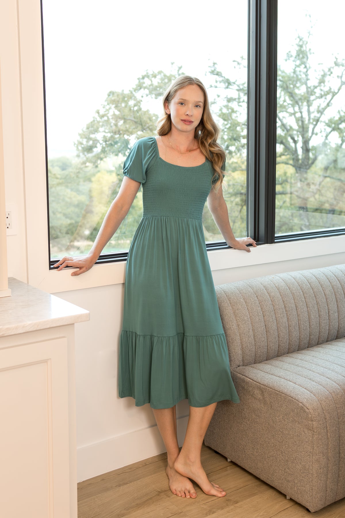 Model wearing Women’s Smocked Dress in Pine standing in a living room