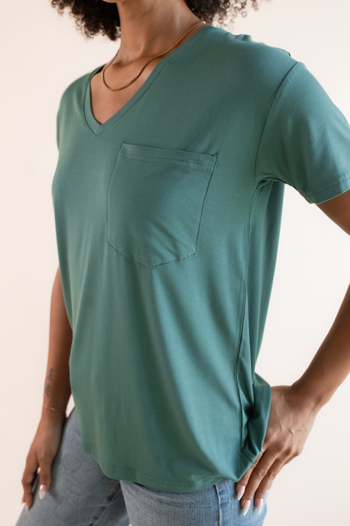 close up of Model wearing Women's Oversized V-Neck Tee in Pine over blue jeans on a beige background