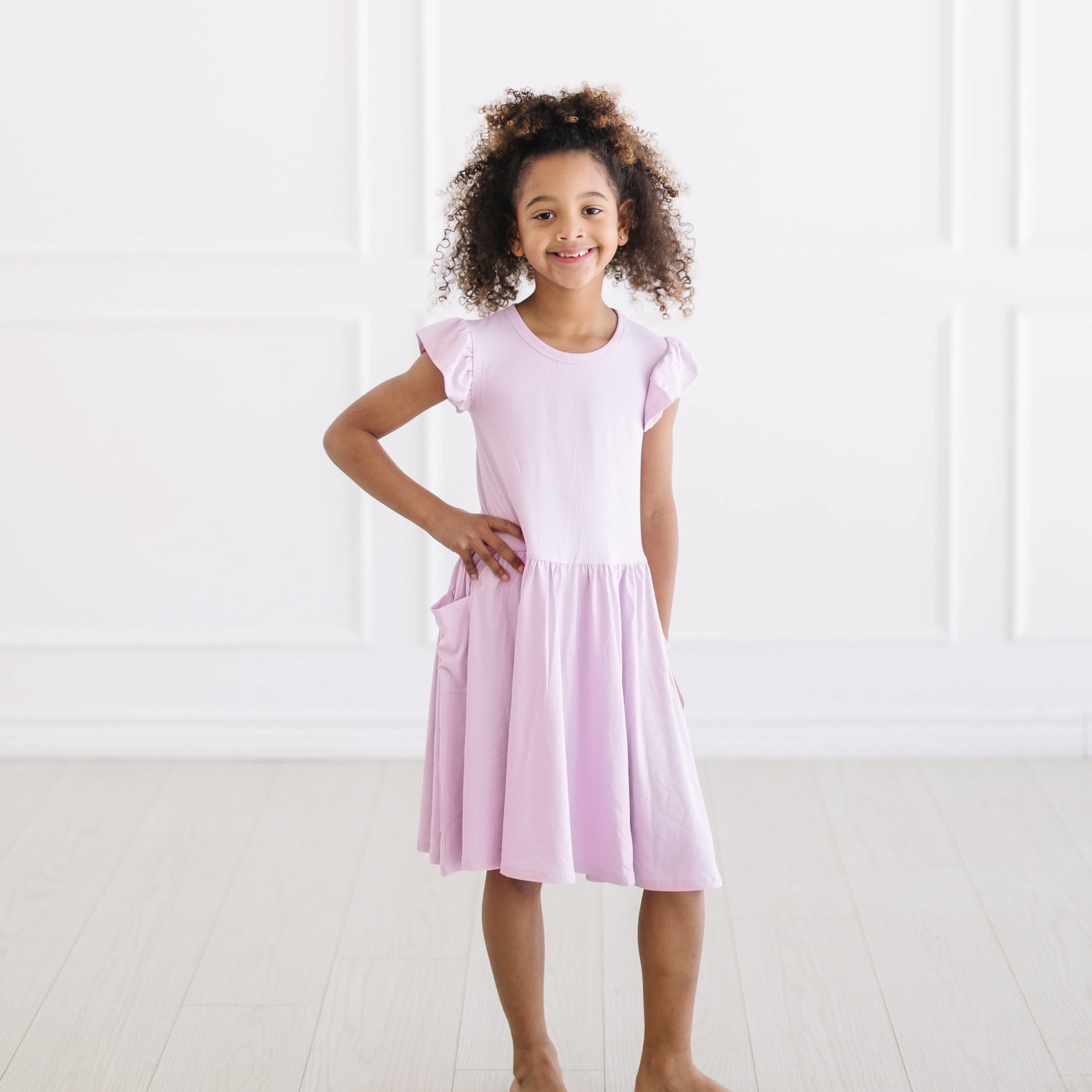Young girl standing with one hand on her hip wearing the Pocket Dress in Thistle