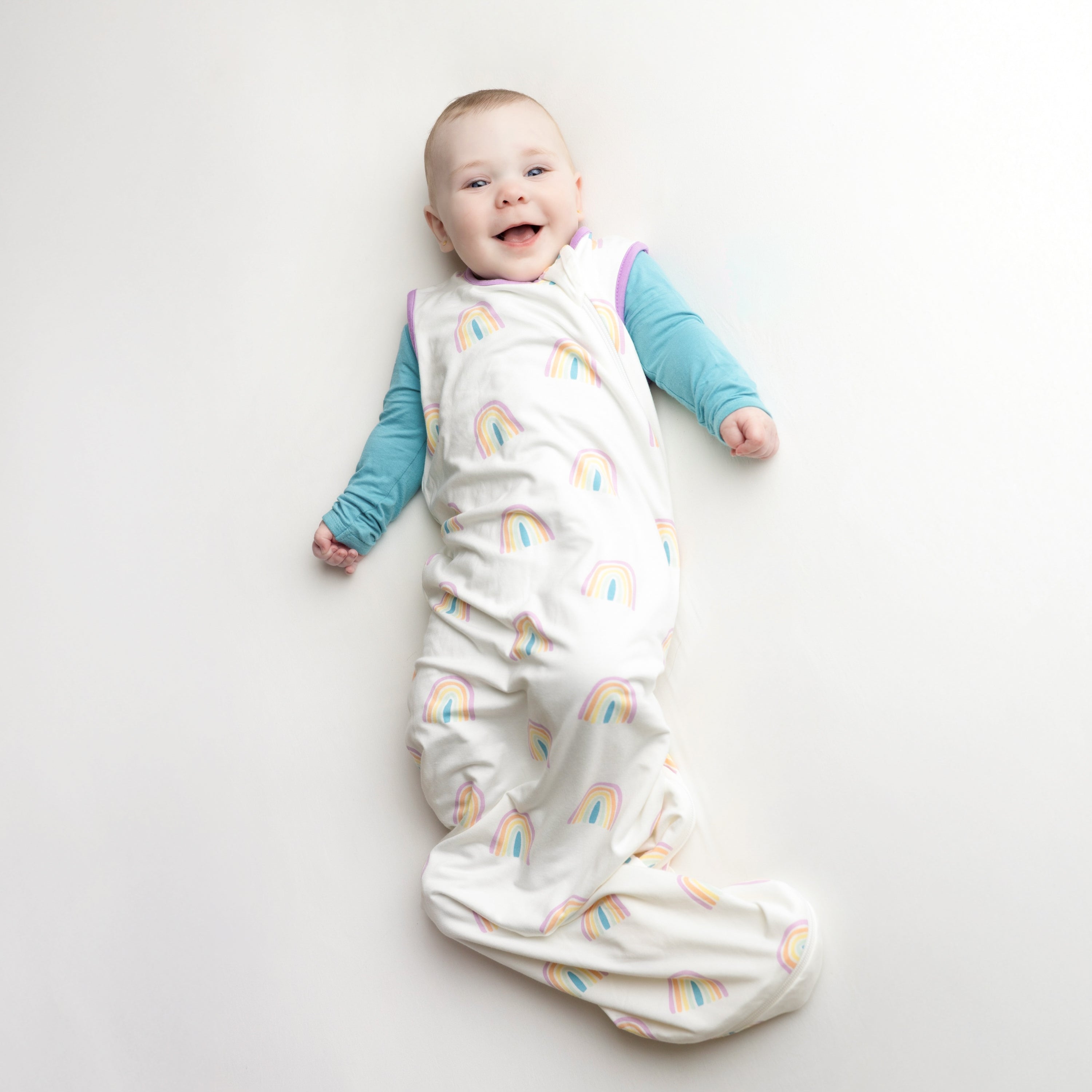 Smiling Baby wearing the Sleep Bag in Poi Rainbow 0.5 with a Makai Romper underneath