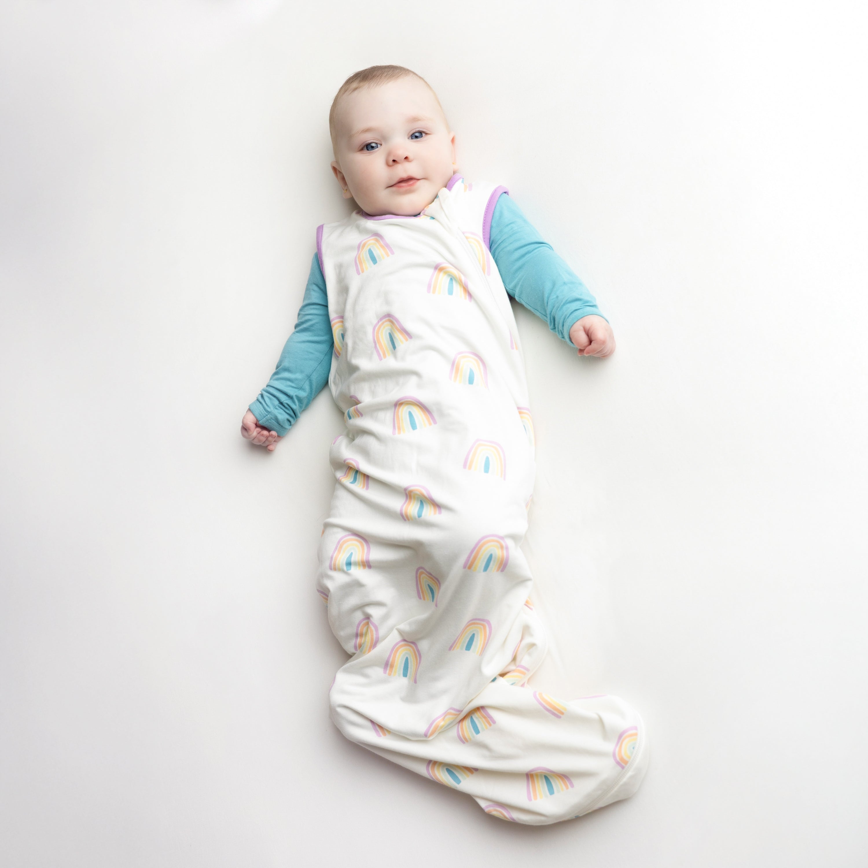 Baby wearing the Sleep Bag in Poi Rainbow 0.5 overtop a Makai long sleeve romper