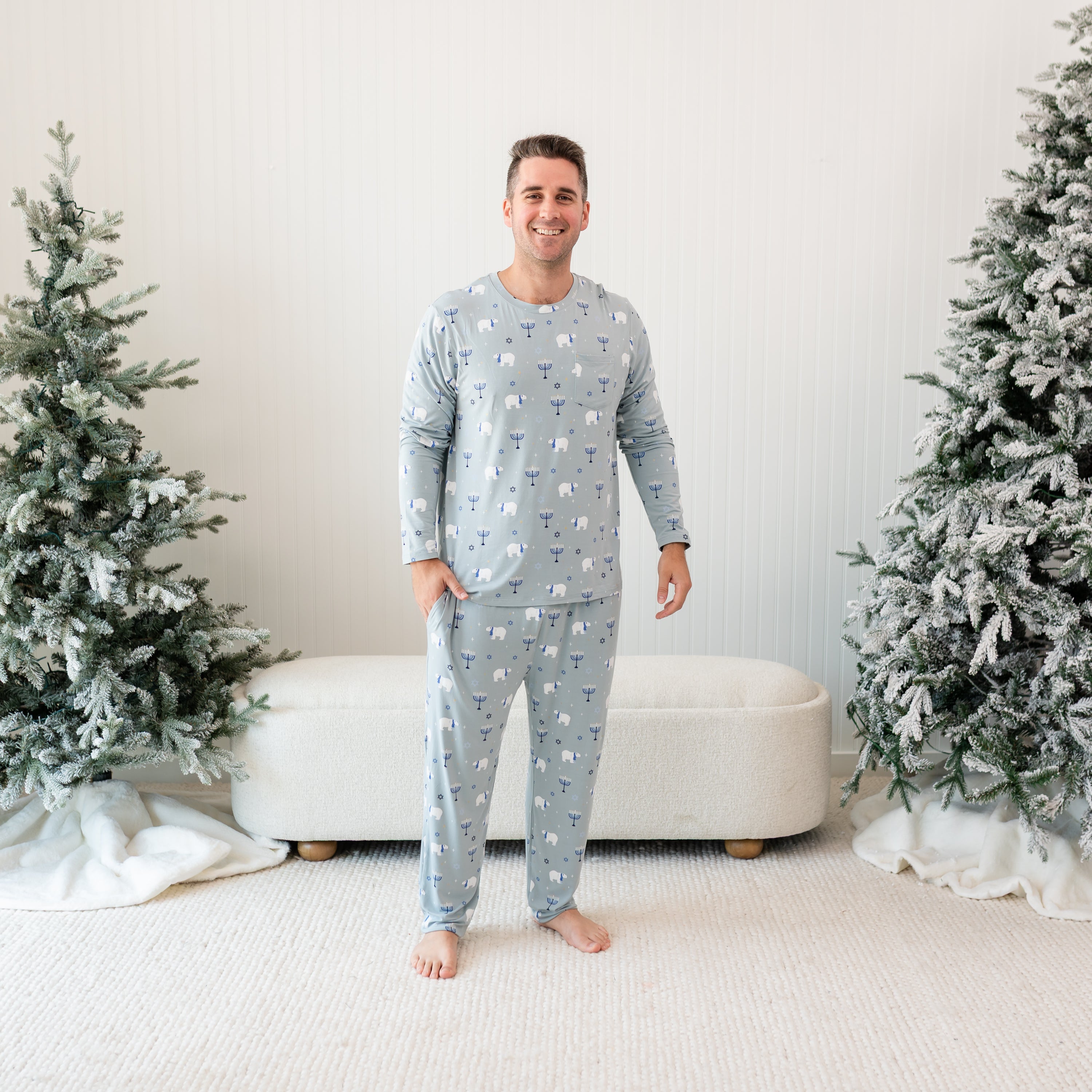 Smiling male model standing between two frosted trees wearing the Men's Jogger Set in Polar Lights with one hand in the pants pocket