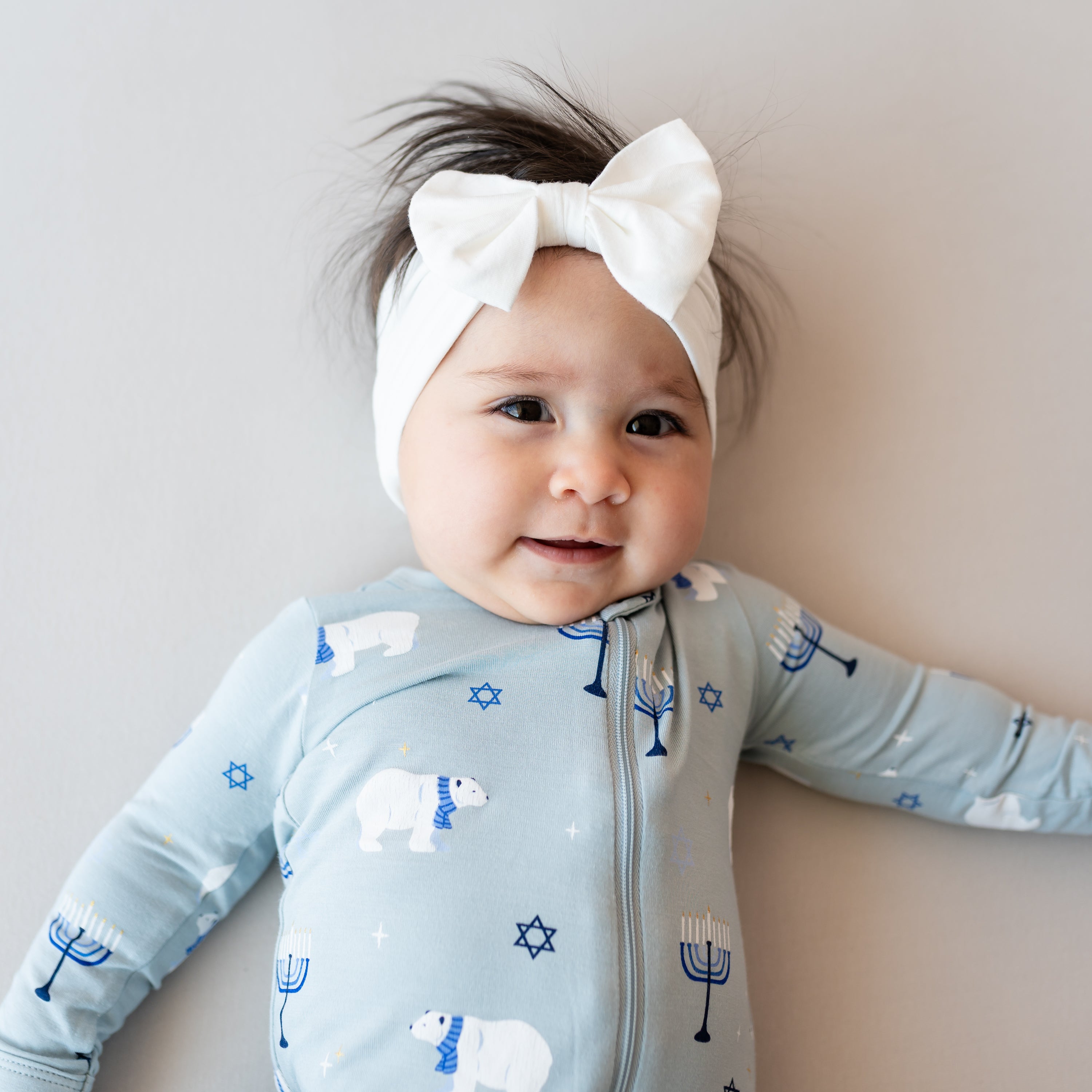Close up of the Zippered Footie in Polar Lights shown on an infant girl paired with a Cloud Bow Headband