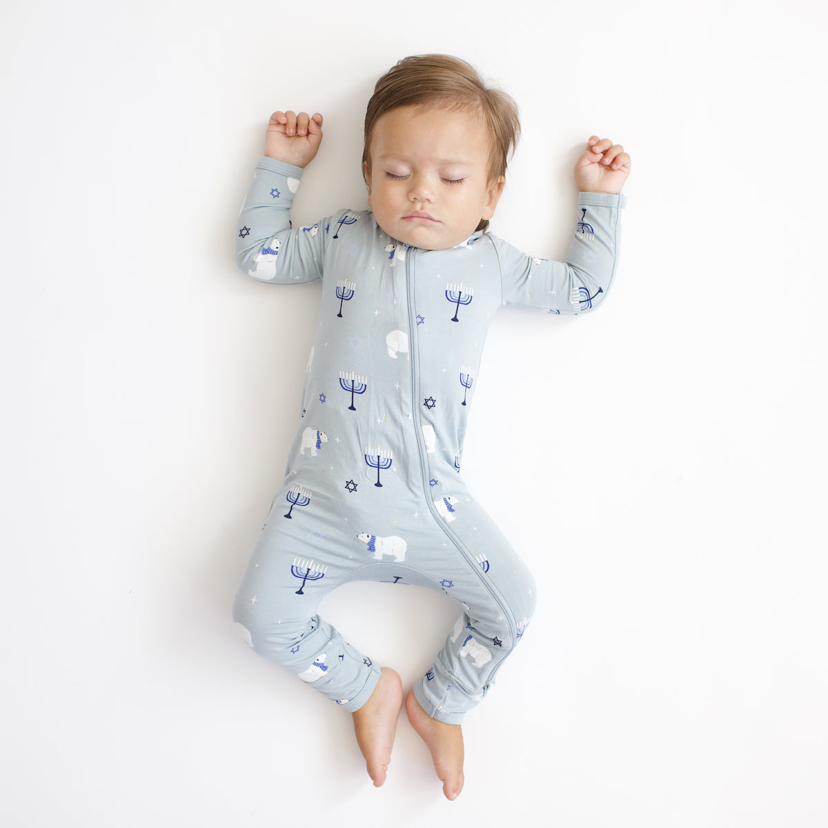 Sleeping toddler wearing the Zippered Romper in Polar Lights laying on a white blanket
