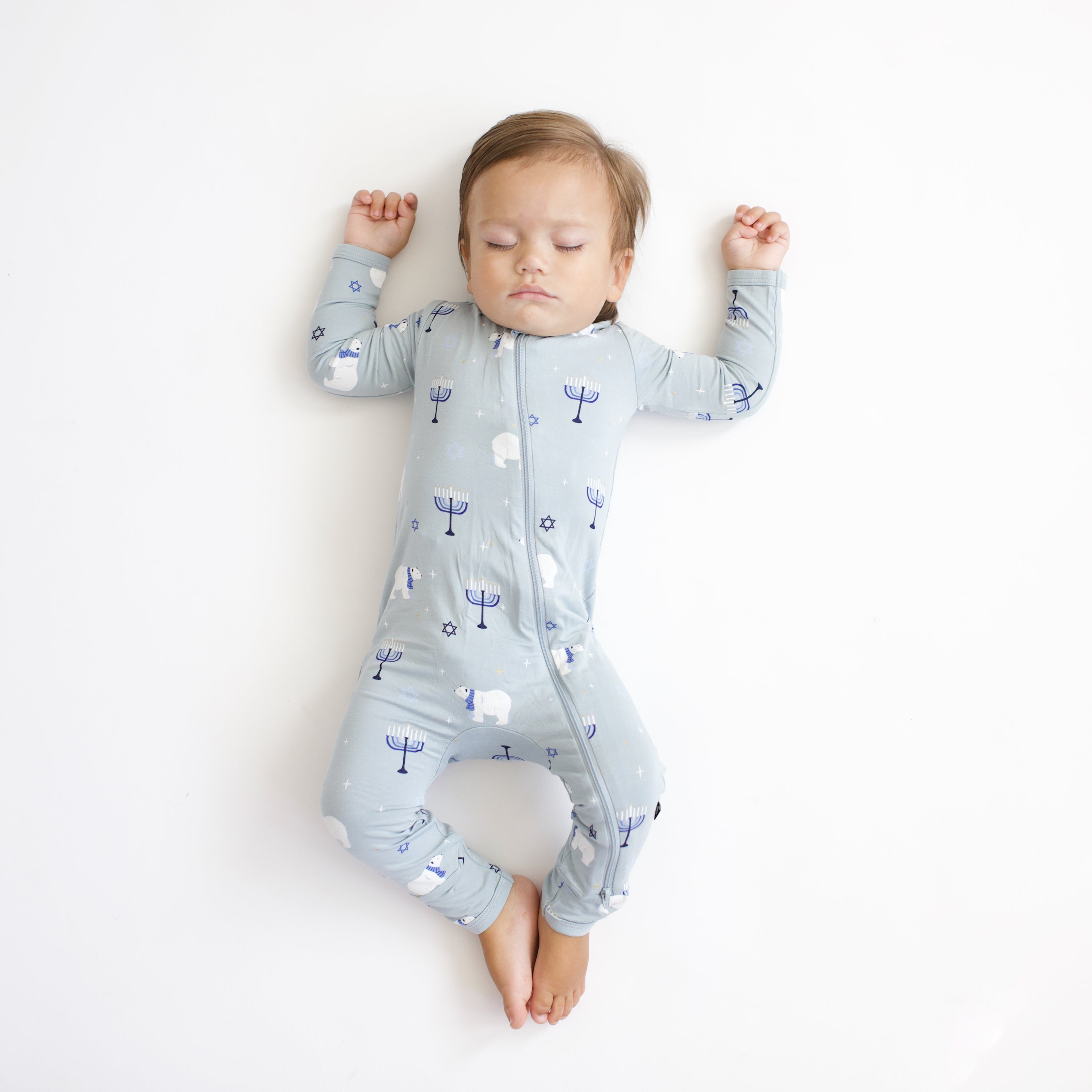 Sleeping infant laying on a white blanket wearing the Zippered Romper in Polar Lights