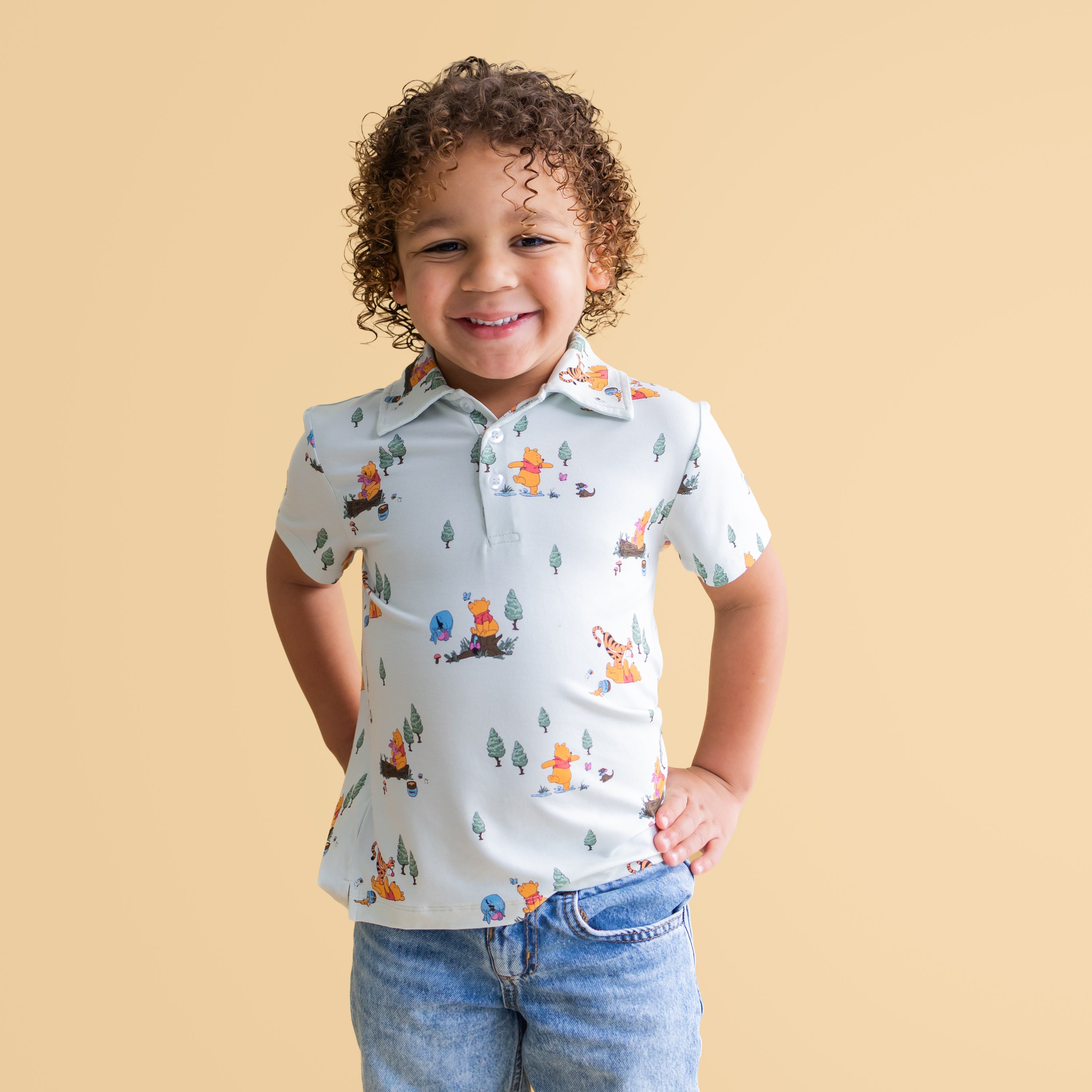 Smiling boy wearing the Toddler Short Sleeve Polo in Winnie the Pooh Hundred Acre Wood paired with jeans